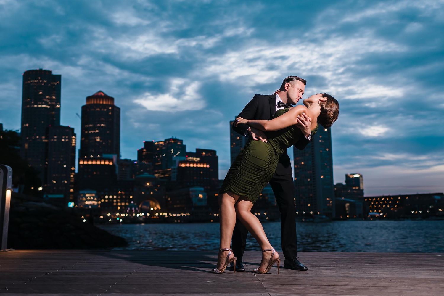 The bride and groom to be pose in a dramatic dip during their engagement session at Fan Pier Park with the Boston Skylin