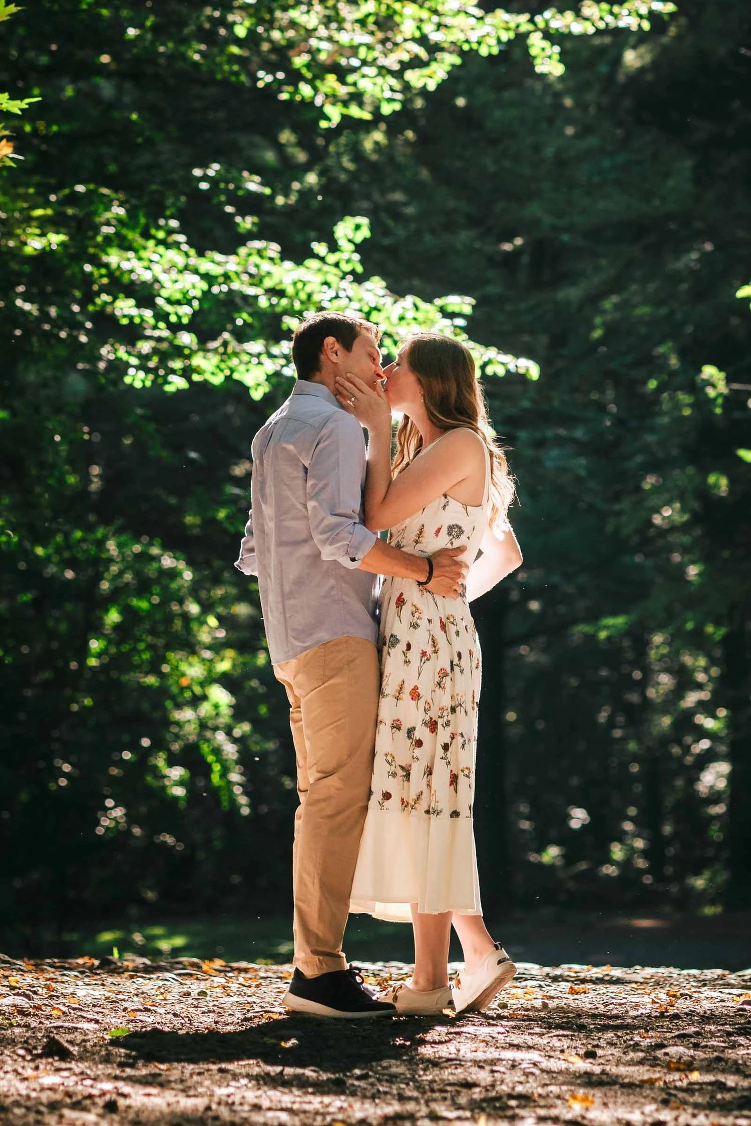 Couple kissing while standing on a fallen log in a sunlit forest clearing. Engagement at Borderland State Park, North Easton, MA