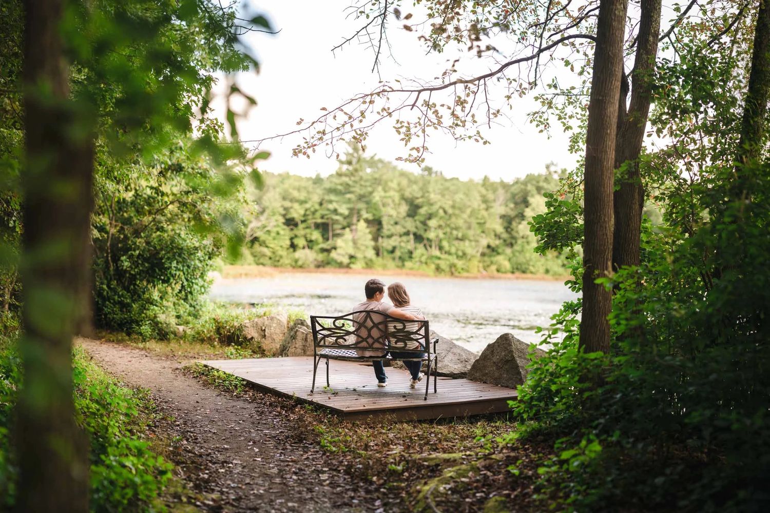 Two people sitting together on a bench overlooking a lake, facing away from the camera in quiet contemplation.  Engagement at Borderland