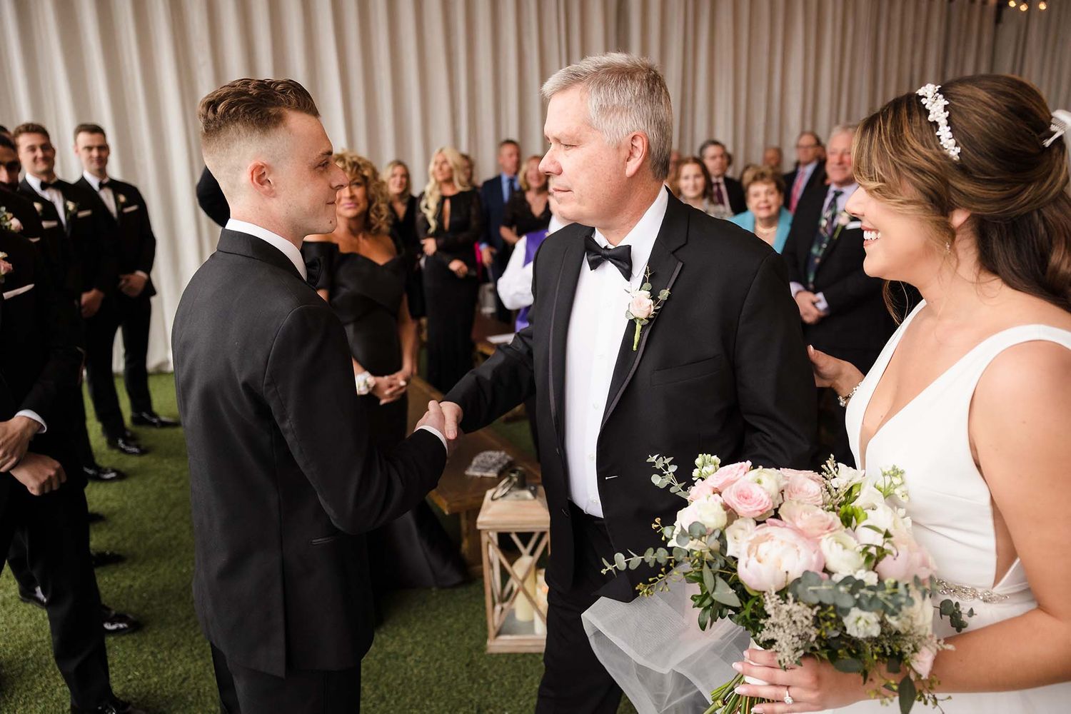 The groom and the father of the bride share a handshake at the start of the wedding ceremony.