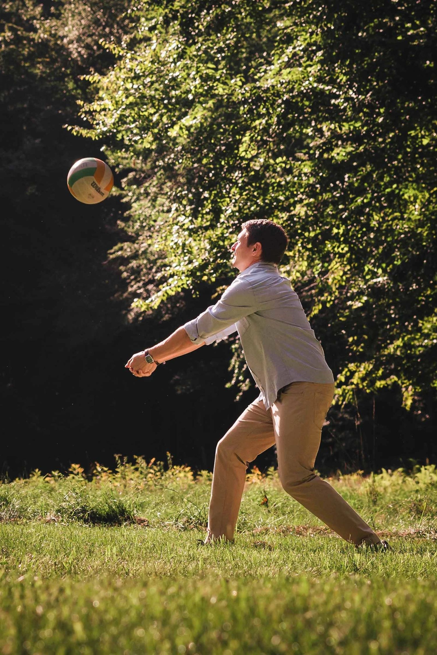 Man in mid-air catching a frisbee in a sunlit grassy field surrounded by trees. Engagement at Borderland State Park, North Easton, MA