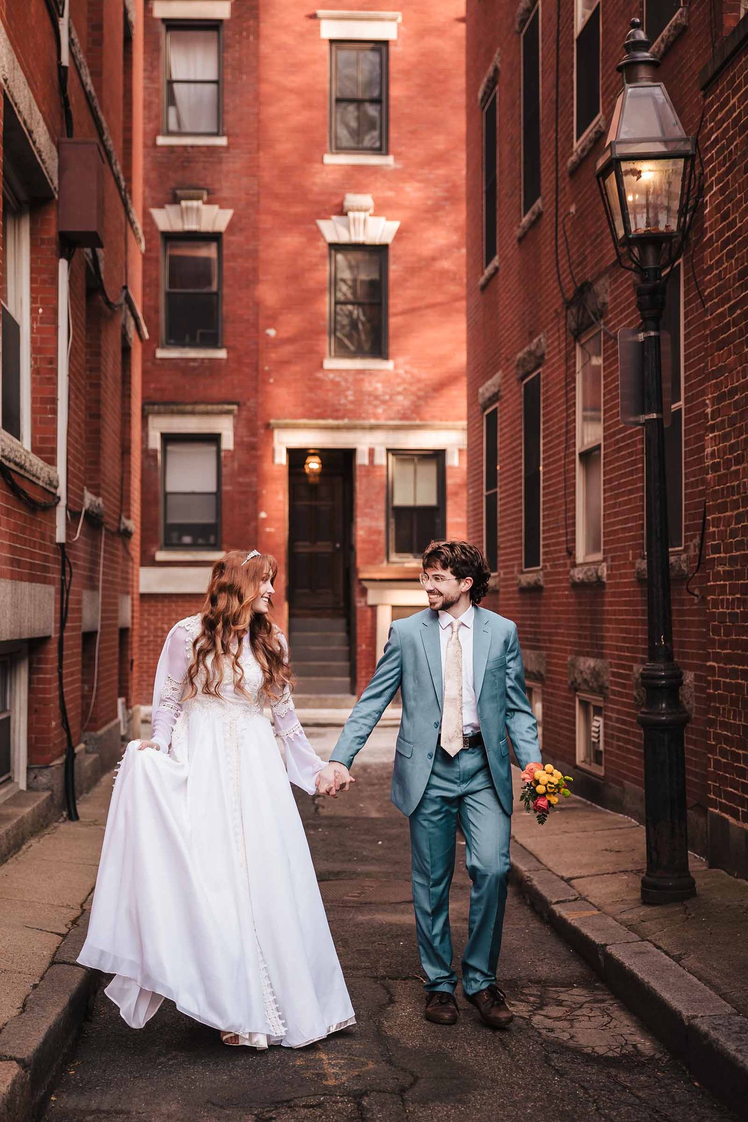 Bride and groom walk hand-in-hand down a brick alley near Boston North End Neighborhood, smiling during their elopement portrait session