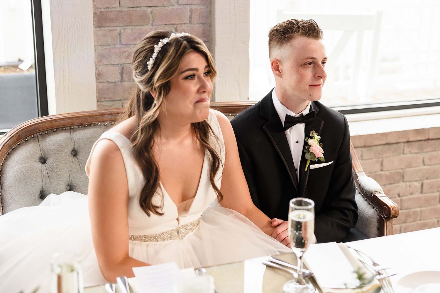 A tear falls down the bride's cheek as she listens with her husband to her father give his wedding reception speech.