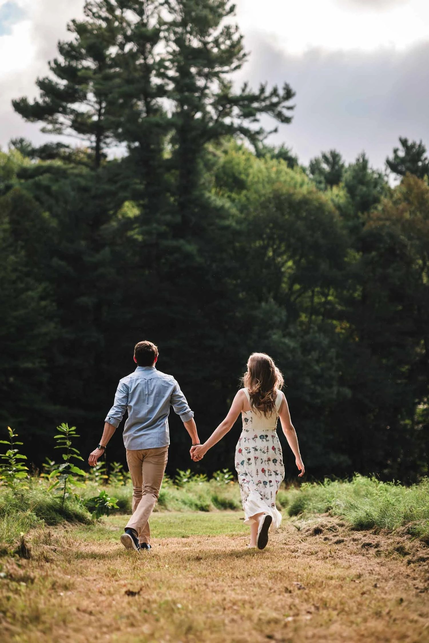 Couple walking hand-in-hand down a dirt path through forested landscape.  Engagement at Borderland State Park, North Easton, MA