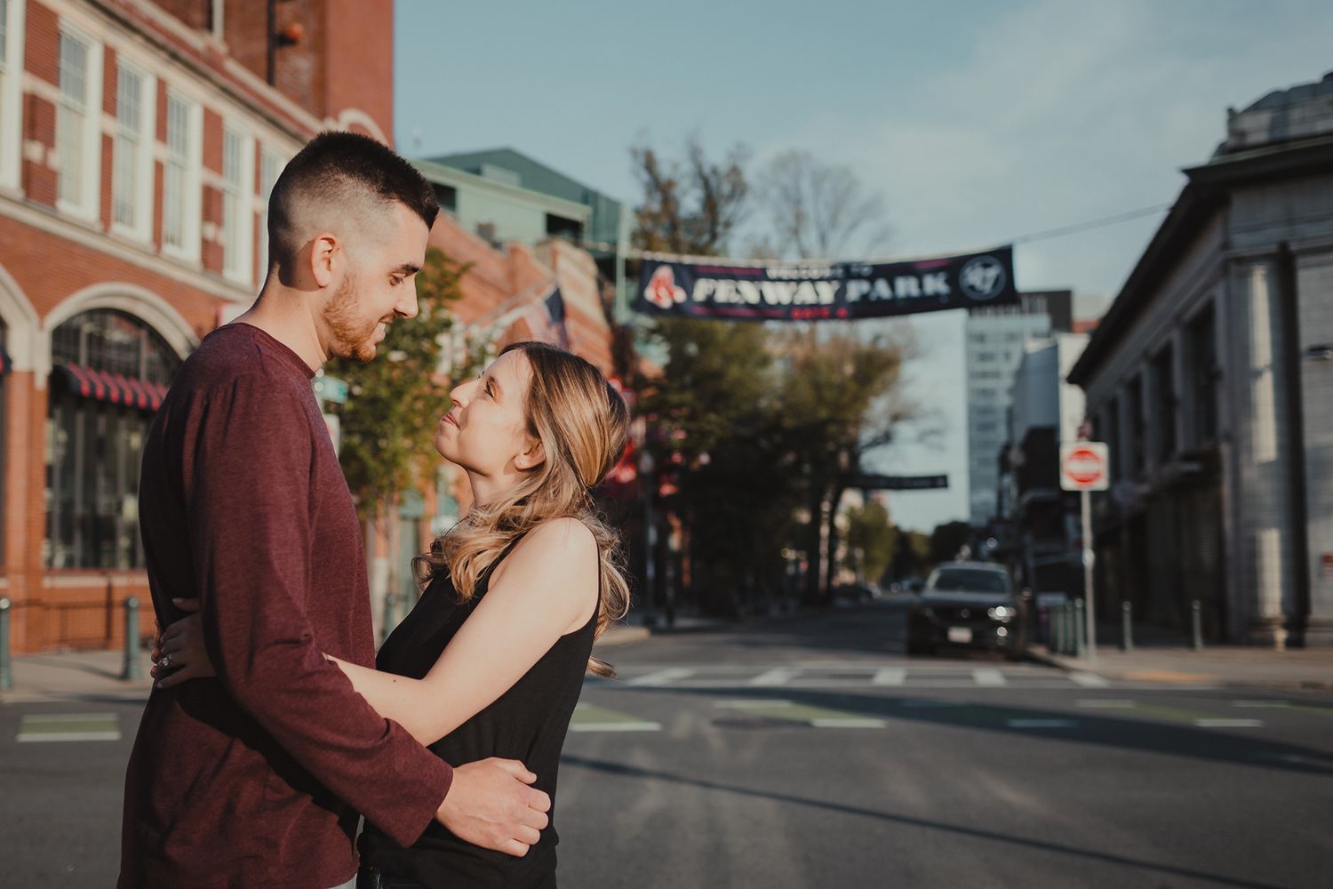The bride and groom hug in front of Fenway Park during their engagement session on a sunny afternoon.
