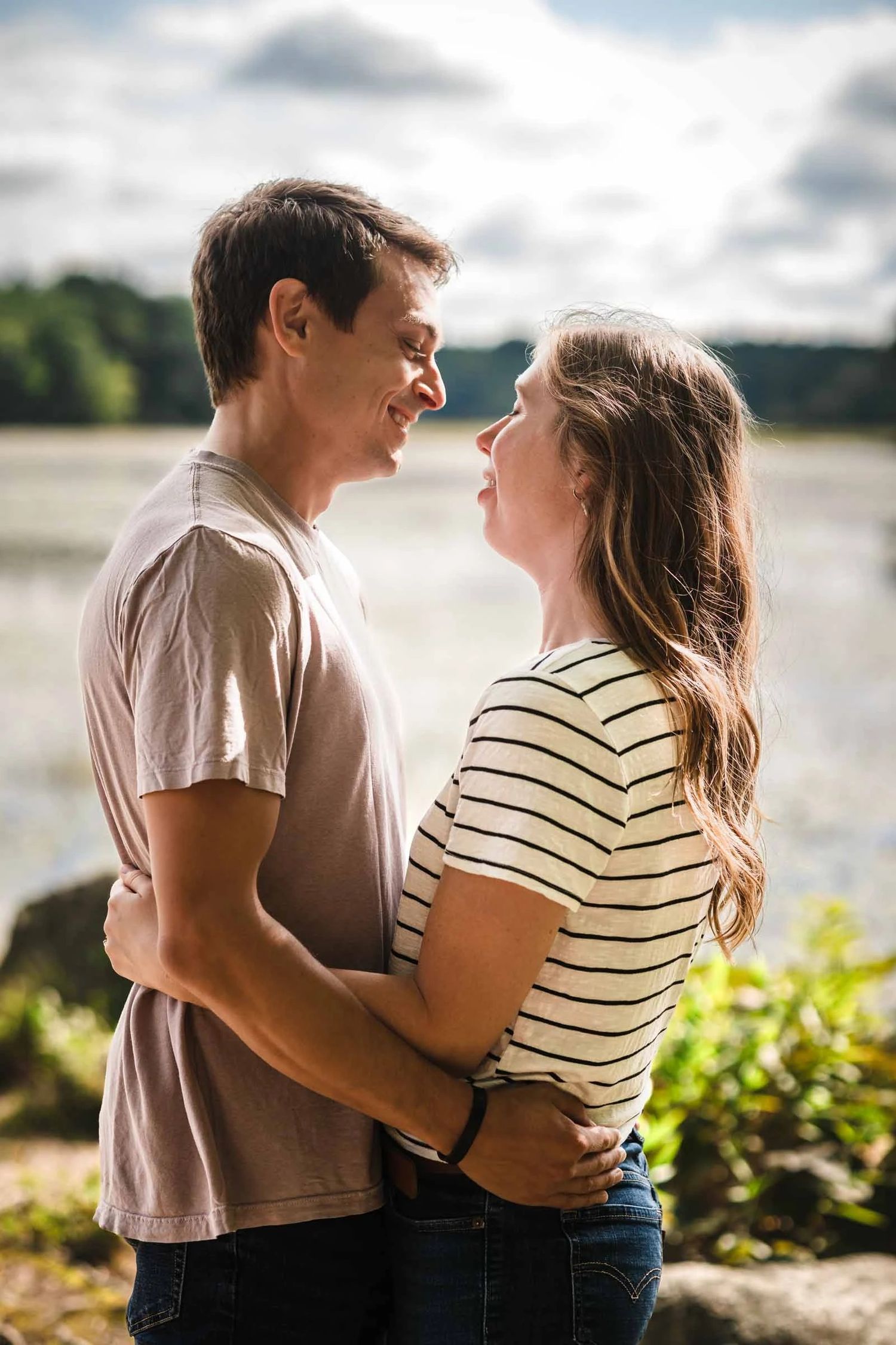 Young couple embracing face-to-face by a riverside, gazing at each other.  Engagement at Borderland State Park, North Easton, MA
