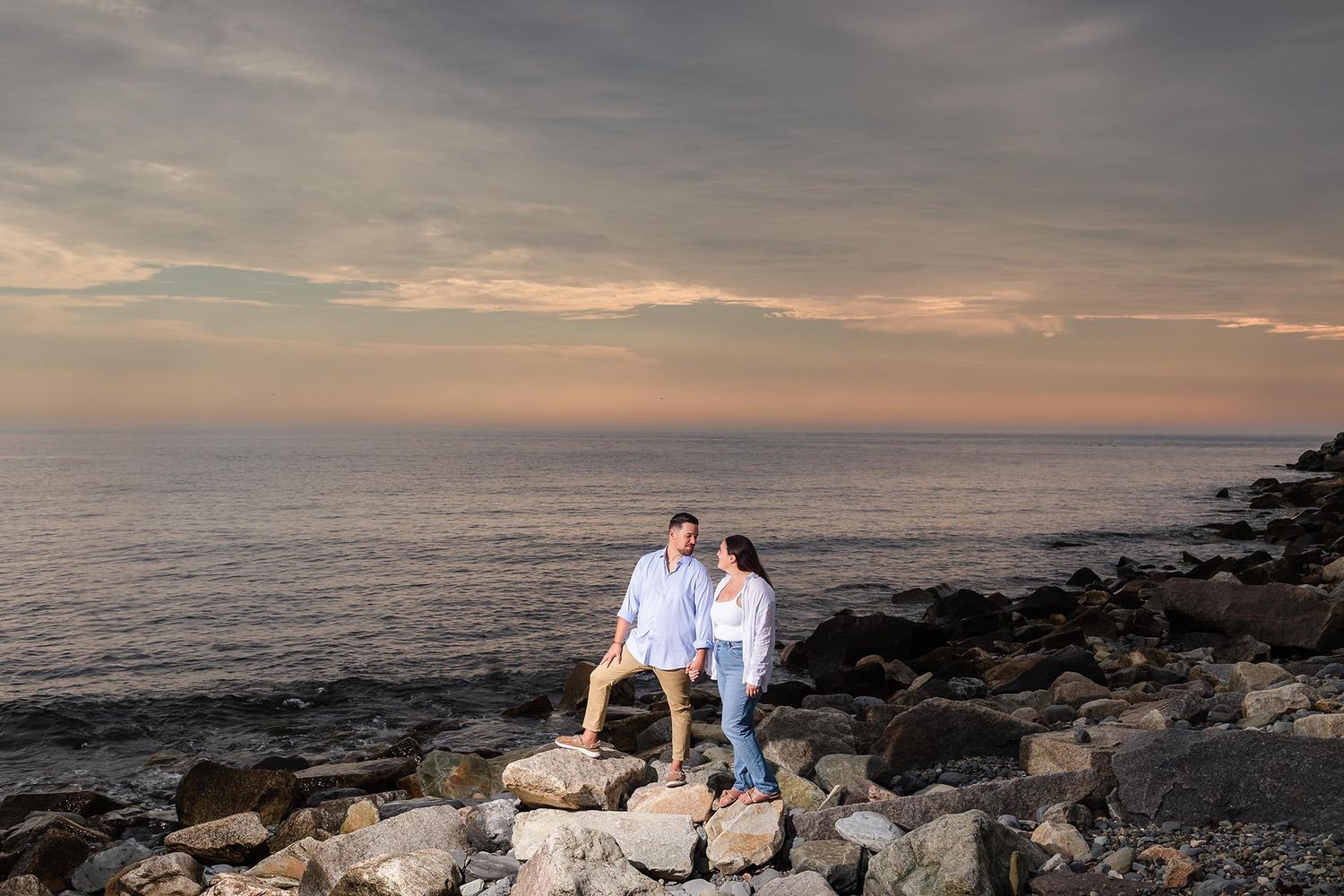 The bride and groom look into each other's eyes  during their engagement session on the beach overlooking the Atlantic