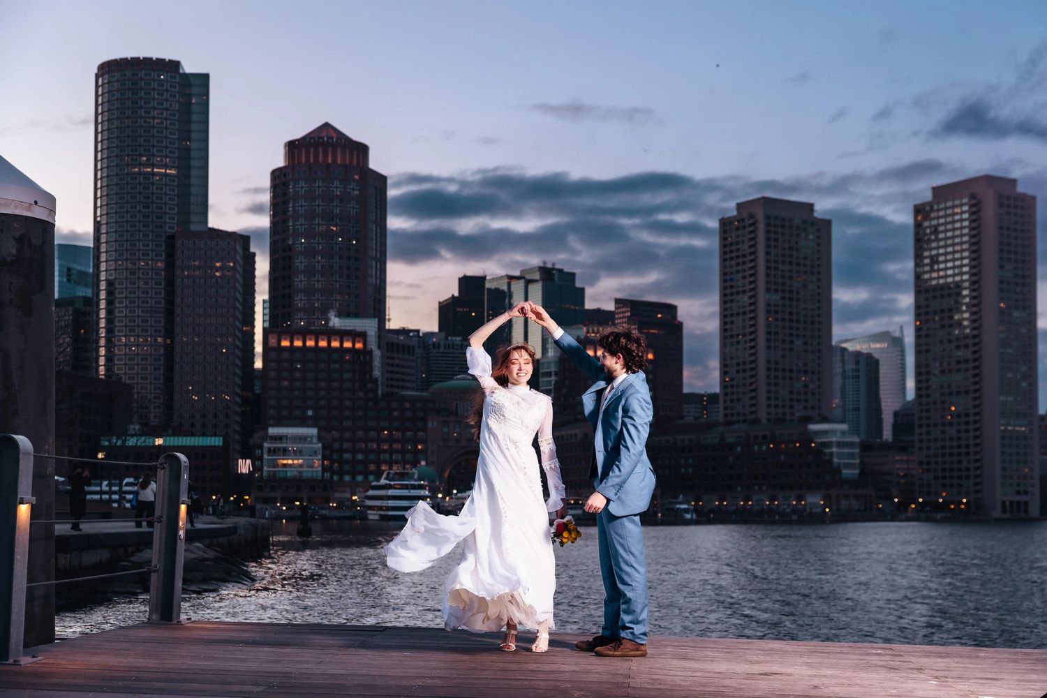 Bride and groom silhouetted against the Boston skyline while dancing together at the marina at Fan Pier Park for their elopement portraits