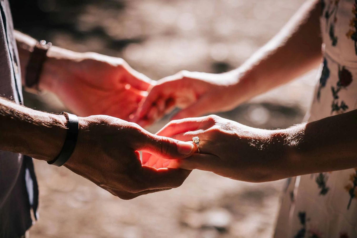 Two people holding hands together, palms touching in intimate gesture with red fabric visible between them. Engagement at Borderland State