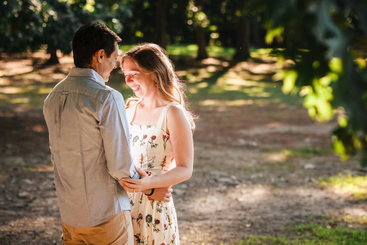 Couple embracing and gazing at each other in dappled sunlight among trees. Engagement at Borderland State Park, North Easton, MA