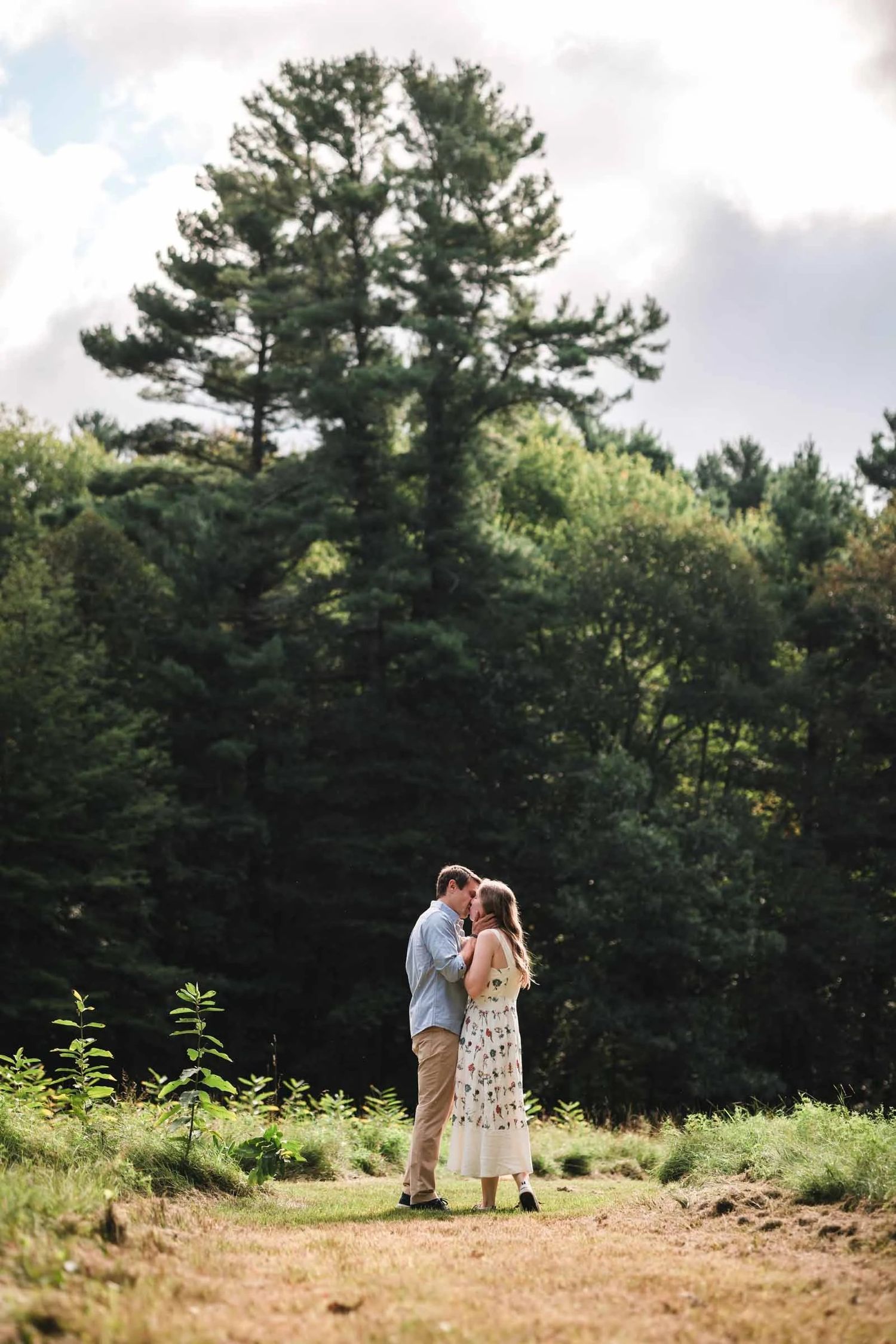 Couple embracing and kissing in a rural field during golden afternoon light.  Engagement at Borderland State Park, North Easton, MA