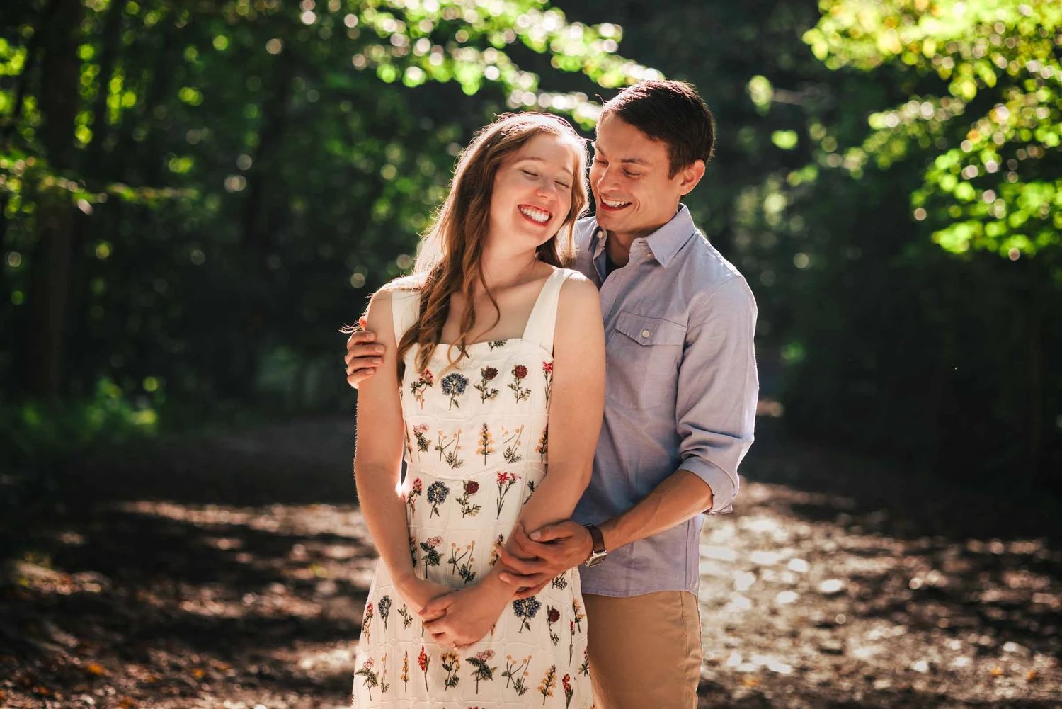 Young couple embracing and smiling together in dappled woodland light. Engagement at Borderland State Park, North Easton, MA