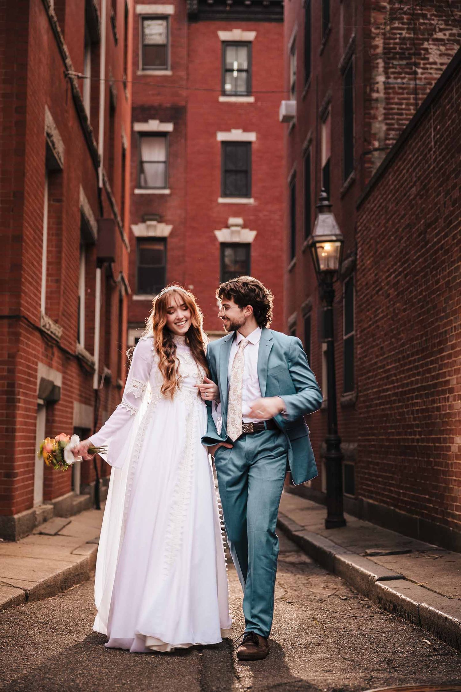 Bride and groom hold hands while walking down a brick alley during their Belmont elopement, gazing at each other