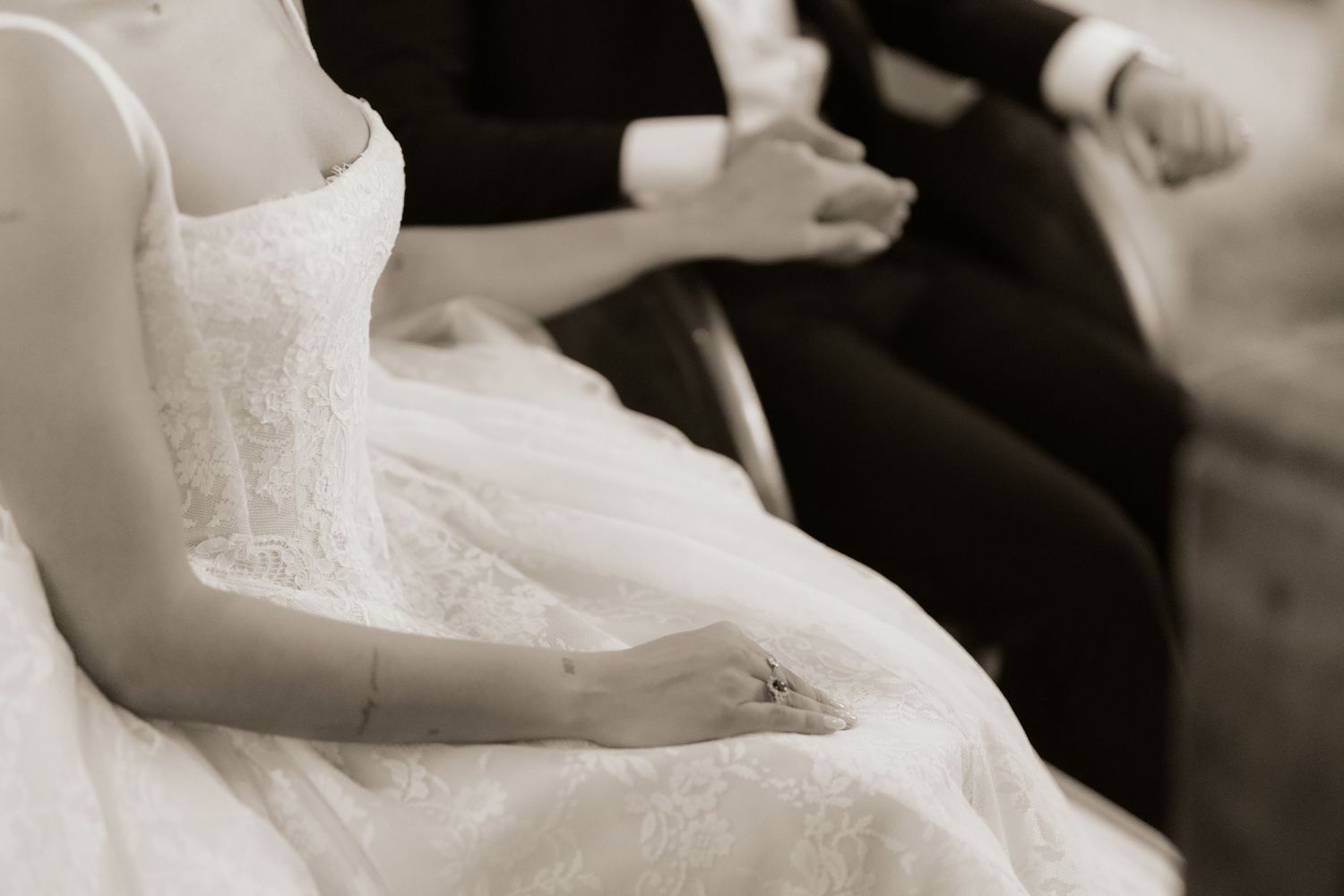 Bride and groom sitting together during wedding ceremony, bride in elegant lace gown, black and white photo.