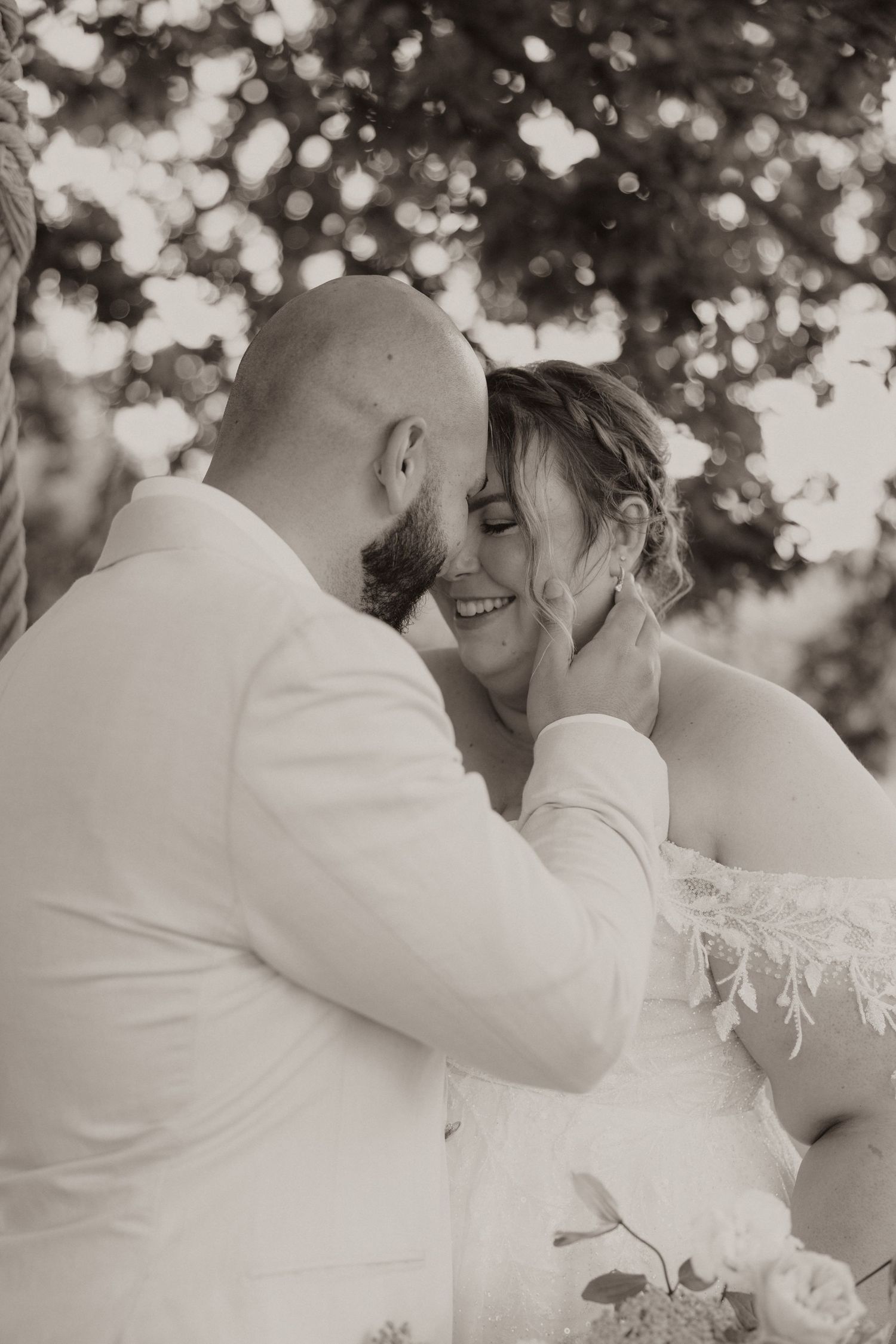 A tender black and white wedding moment captured outdoors with soft bokeh lighting in the background.