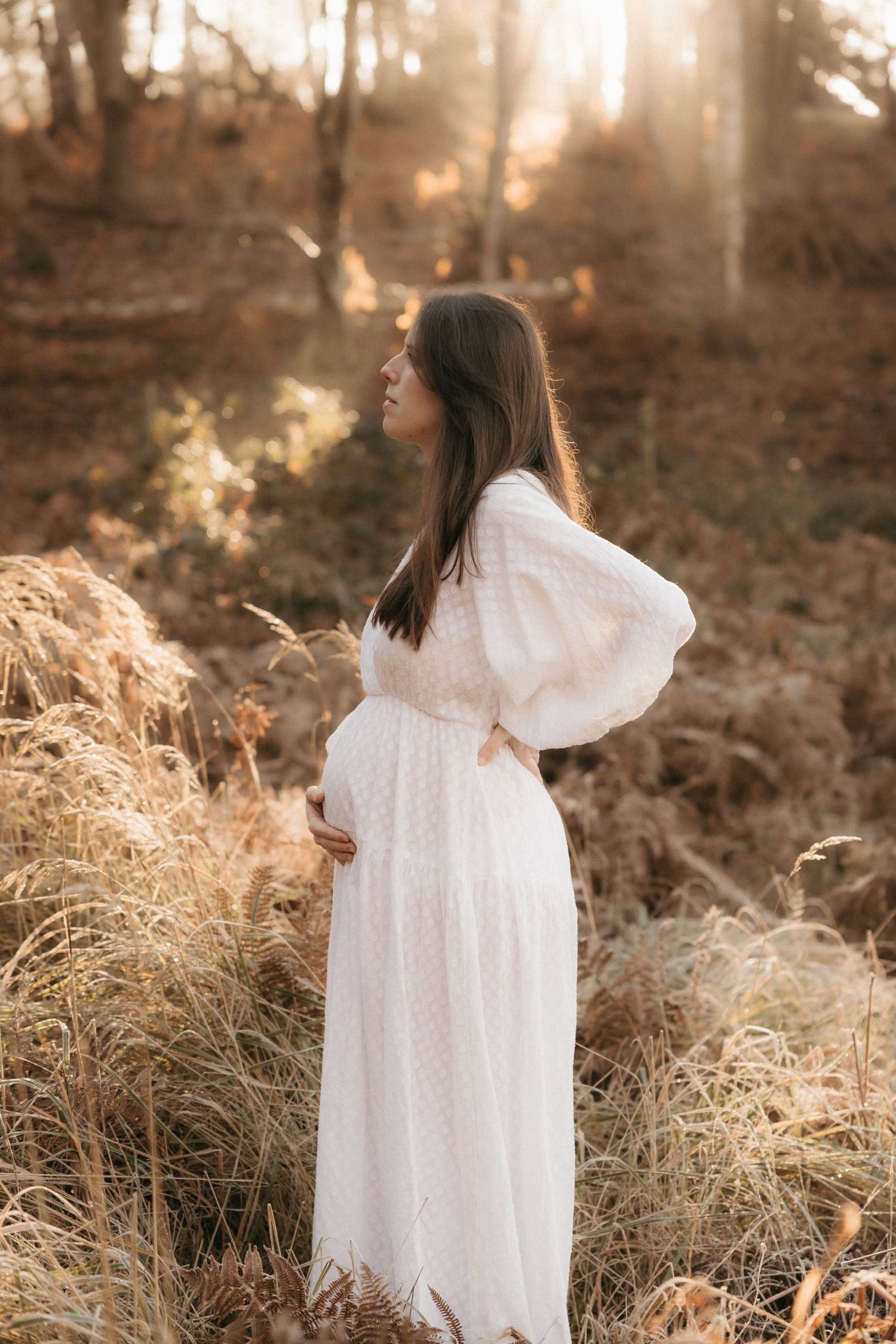 Person in flowing white dress walking through tall golden grass in sunlit forest.