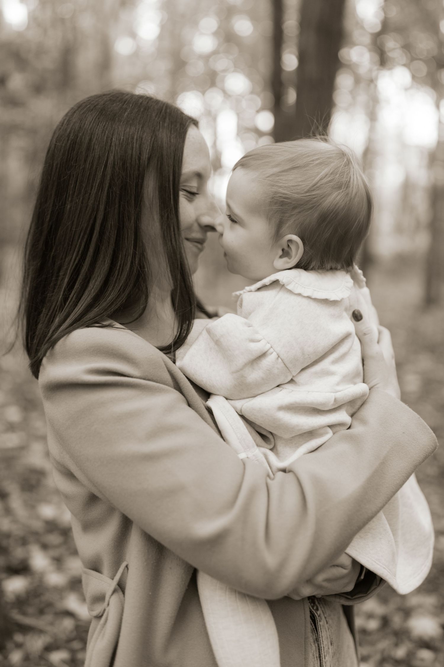 A tender moment between parent and baby captured in sepia tones during an autumn day in the woods.