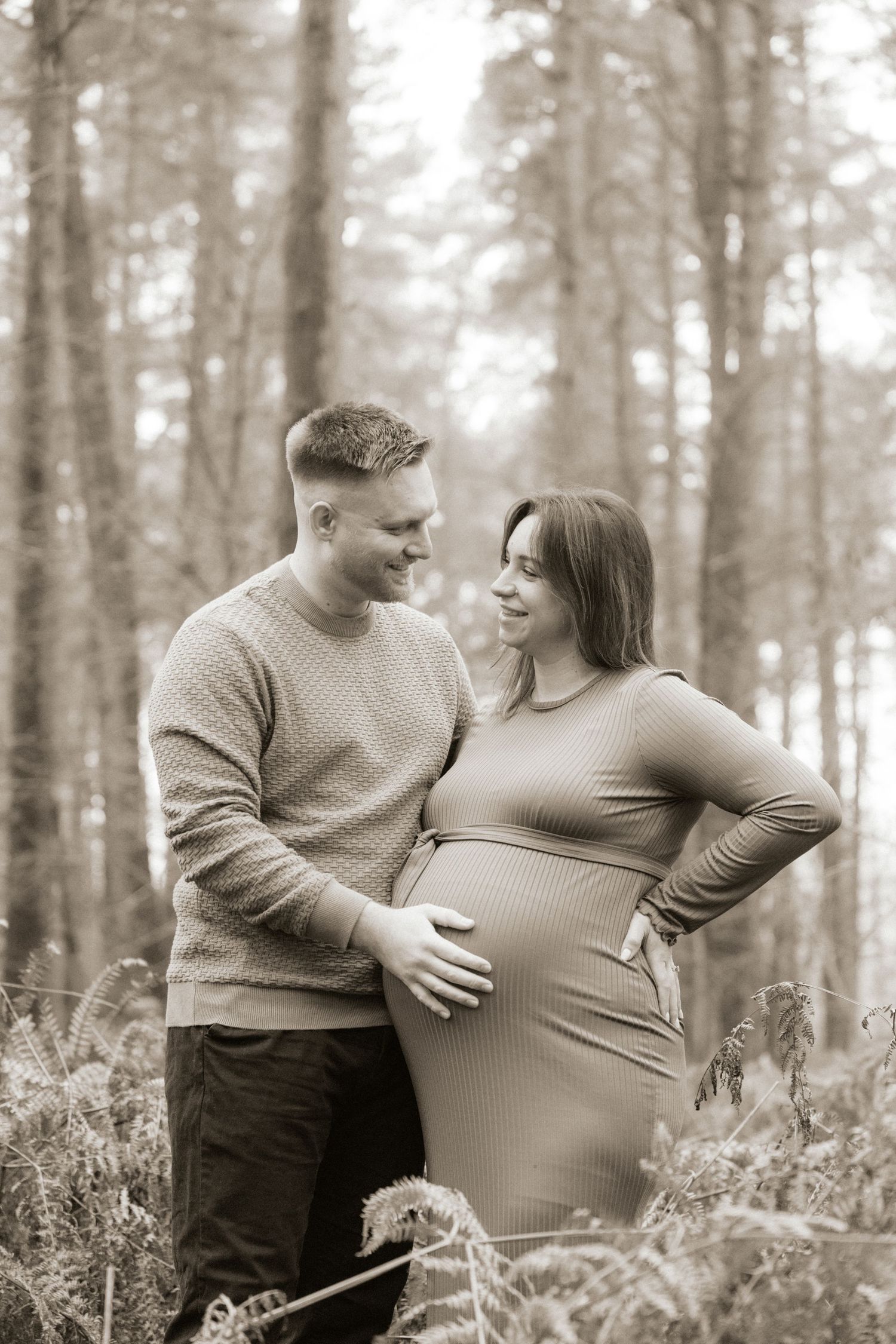 A couple shares an intimate moment in a misty forest setting during a maternity photoshoot.