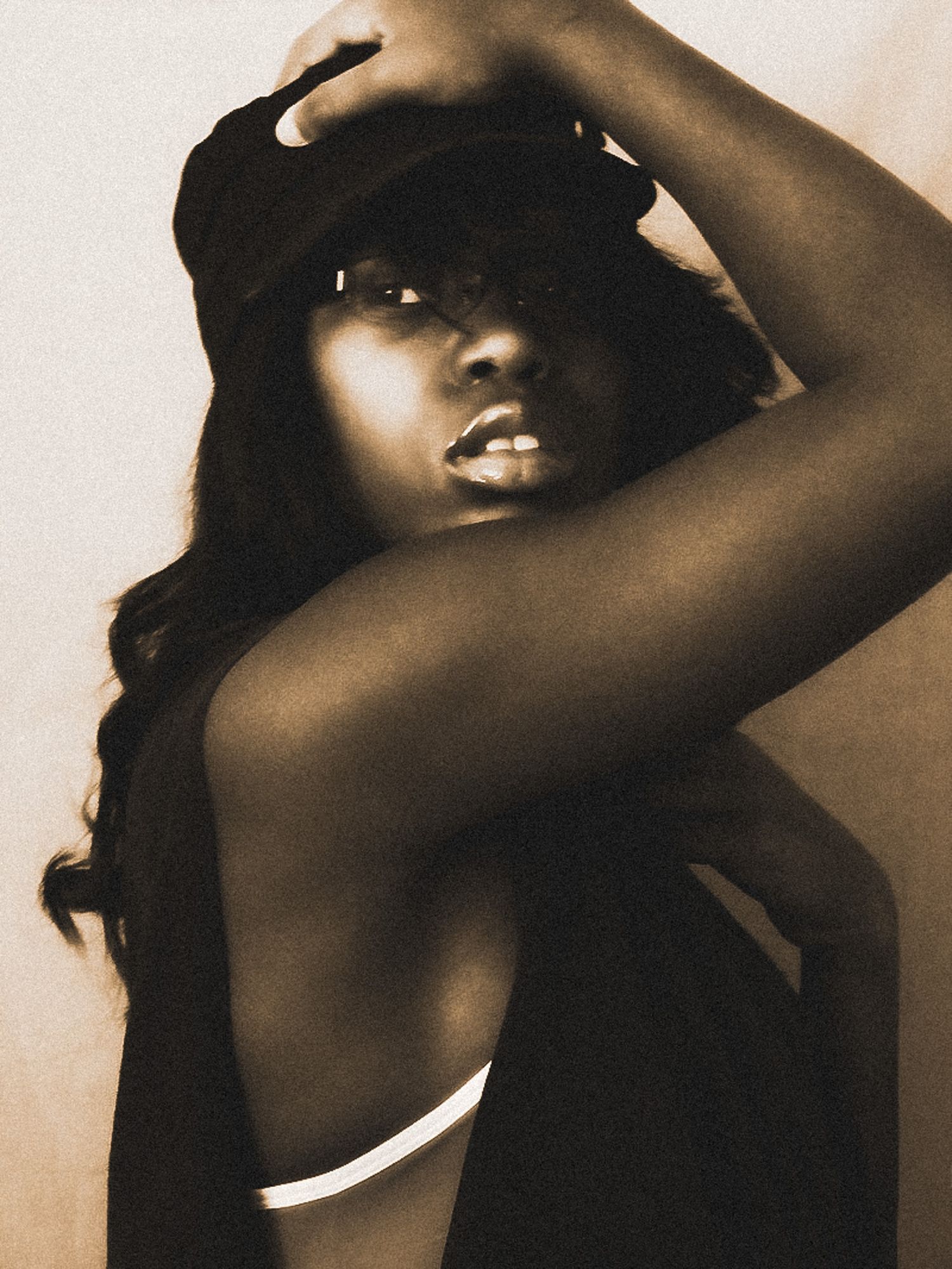 Sepia toned artistic portrait of a woman adjusting her cap in a dramatic pose.