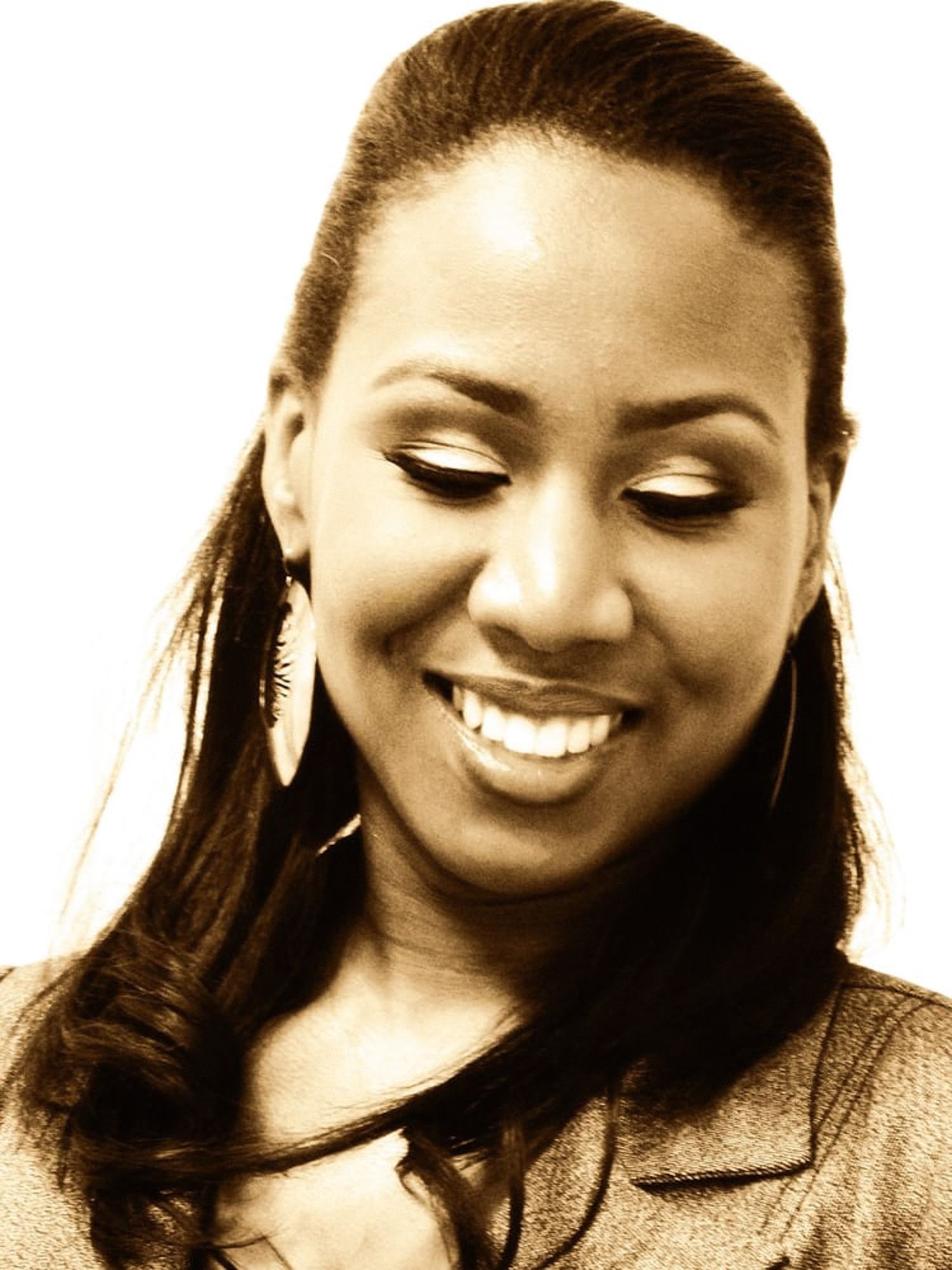 Sepia toned portrait of a smiling woman with hoop earrings and elegant makeup looking down.