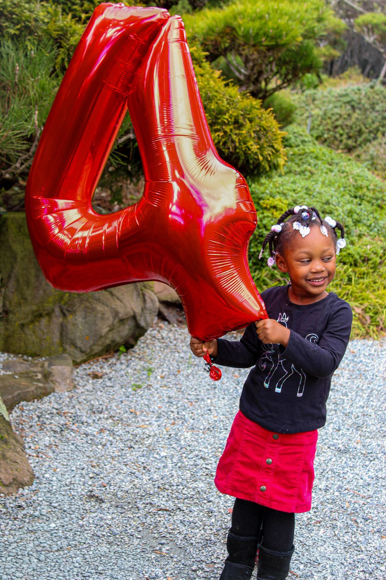 Happy young girl holding a large red number 4 balloon, celebrating her 4th birthday outdoors.