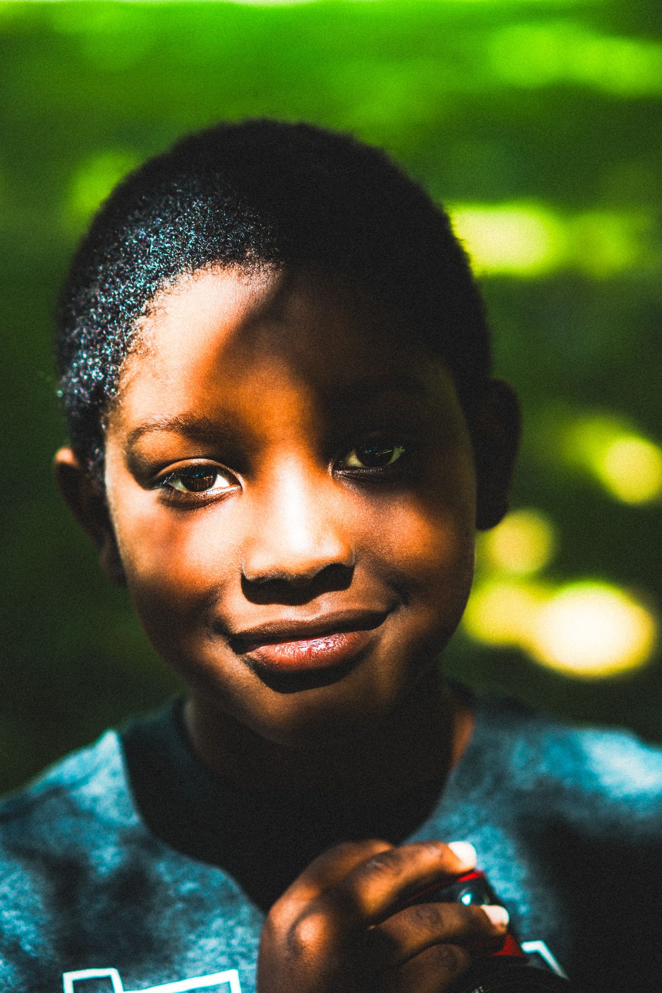 Close-up portrait of a young boy with short hair smiling softly against a green bokeh background.