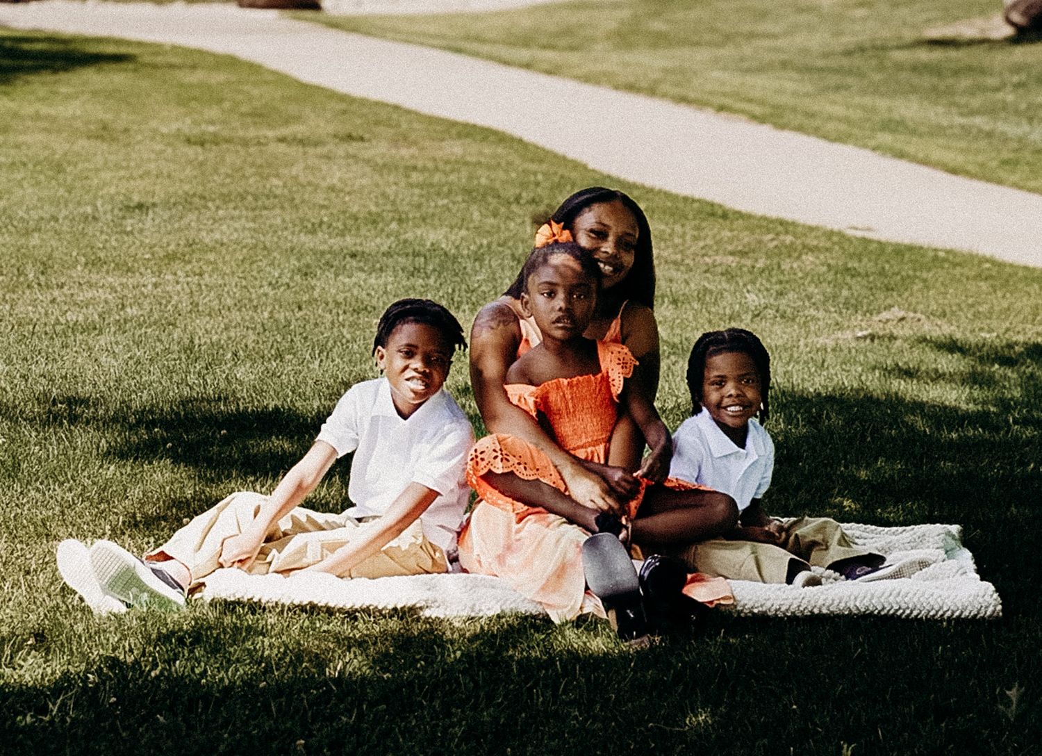 Black mother and three children smiling together on a blanket in a sunny park.
