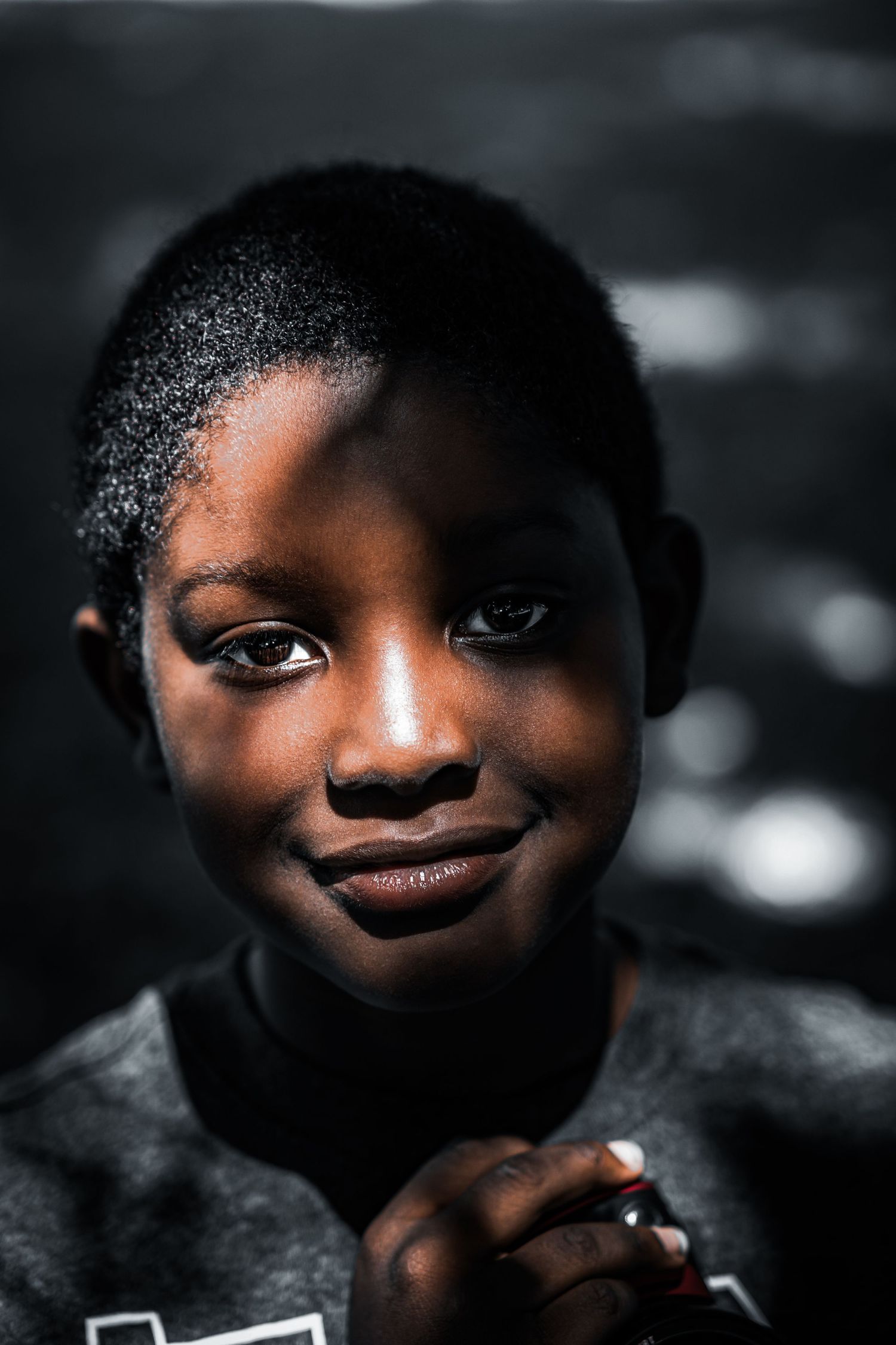 A young Black boy with short hair smiles warmly at the camera against a dark background.