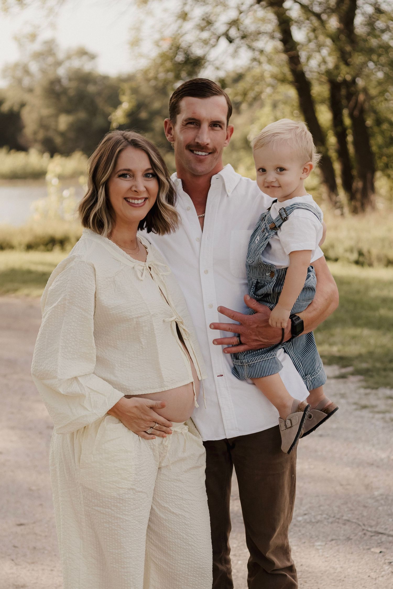 Family smiling together by a lake during outdoor photos in Hastings, Nebraska