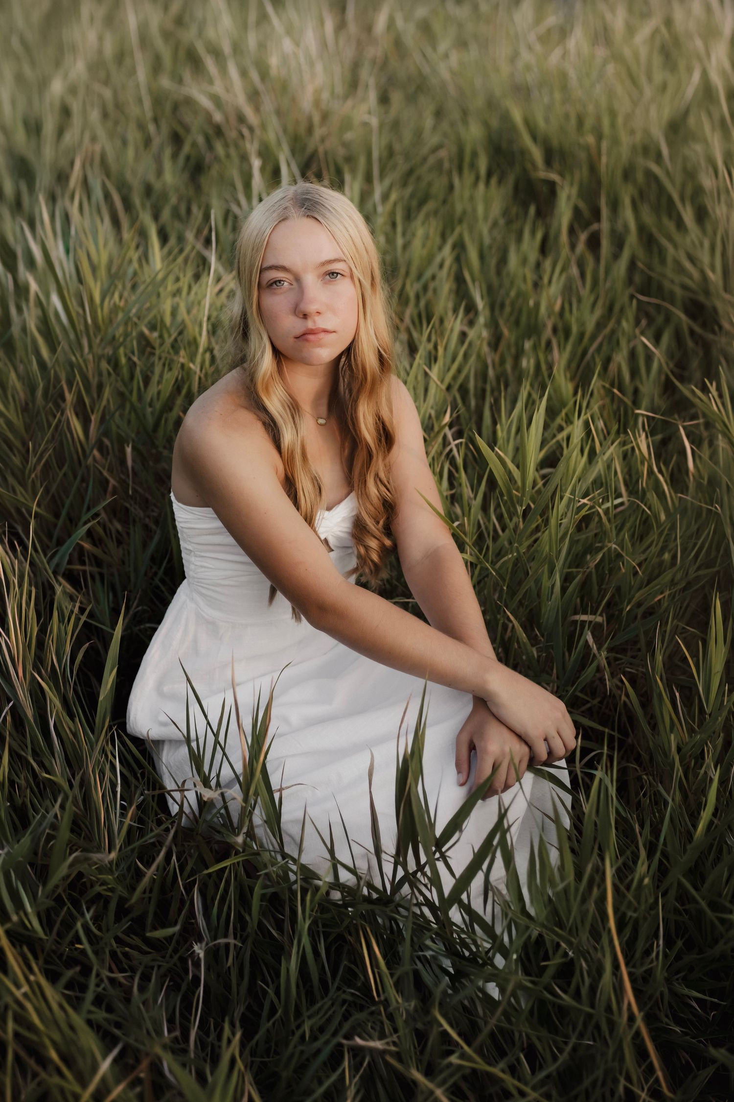 Senior girl sitting in a field during golden hour senior portraits