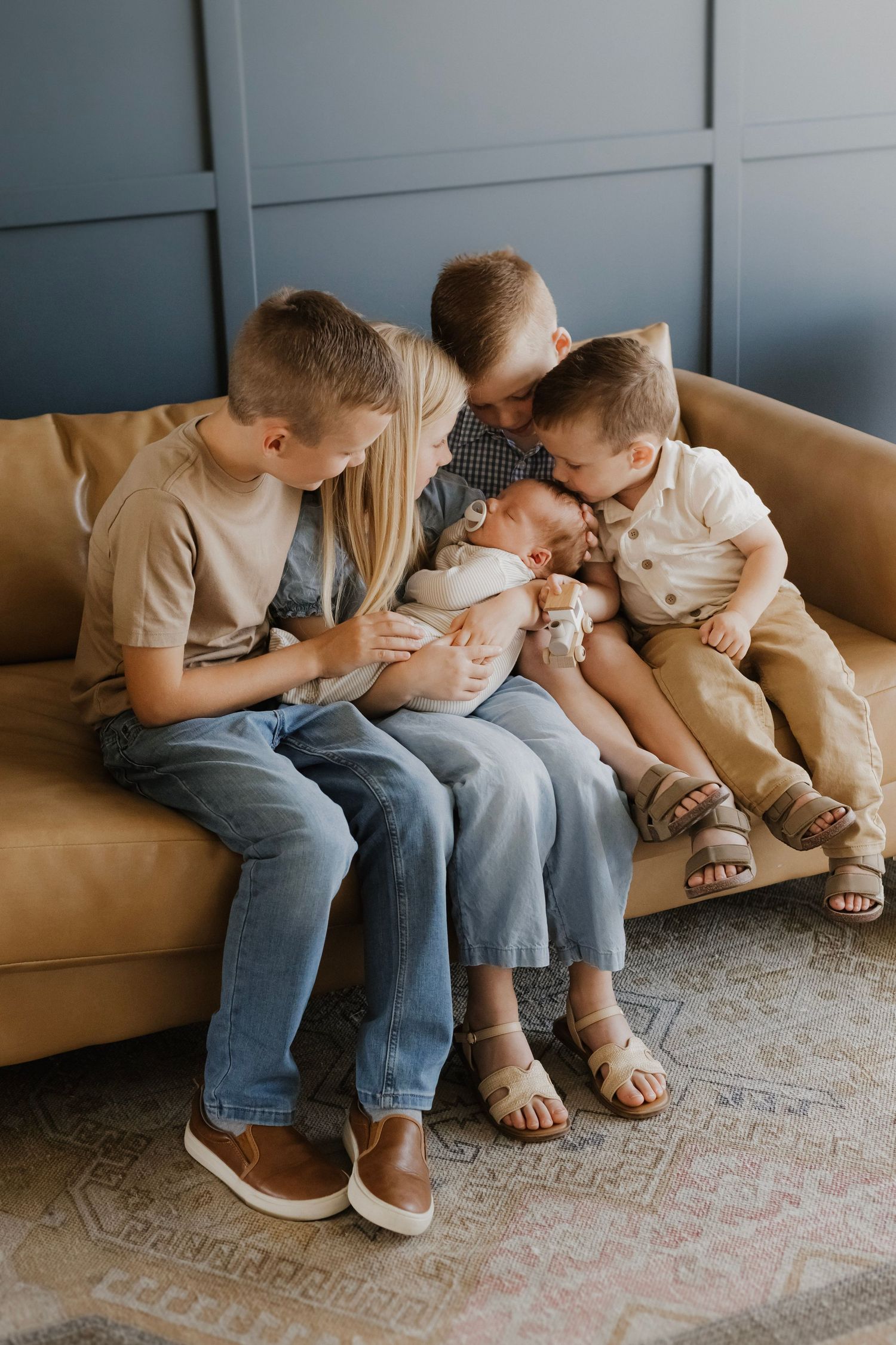 Four siblings sitting on a couch and embracing their newborn sibling during an in-home newborn lifestyle session