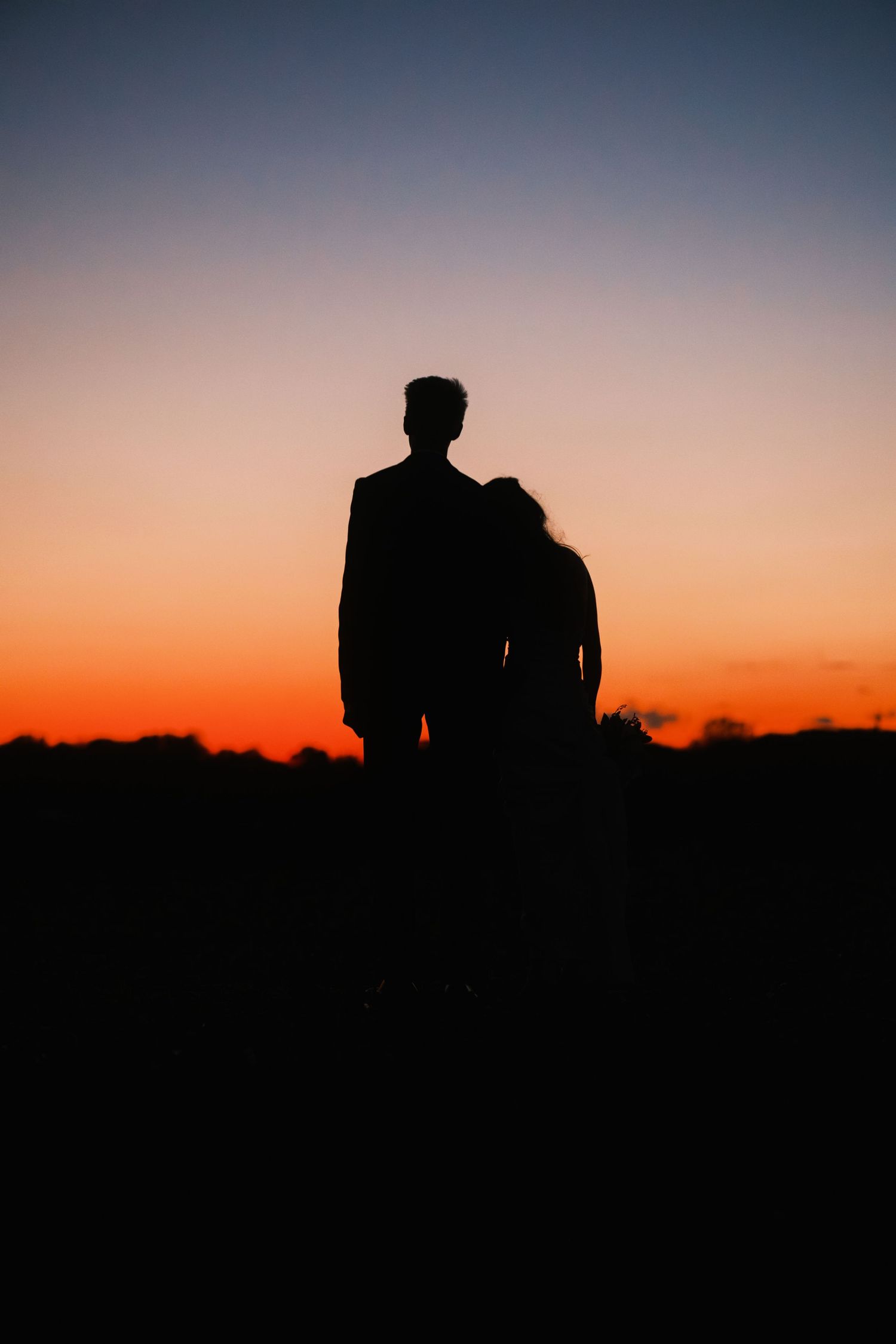 Silhouette of wedding couple standing together against a stunning vibrant orange and red sunset sky.