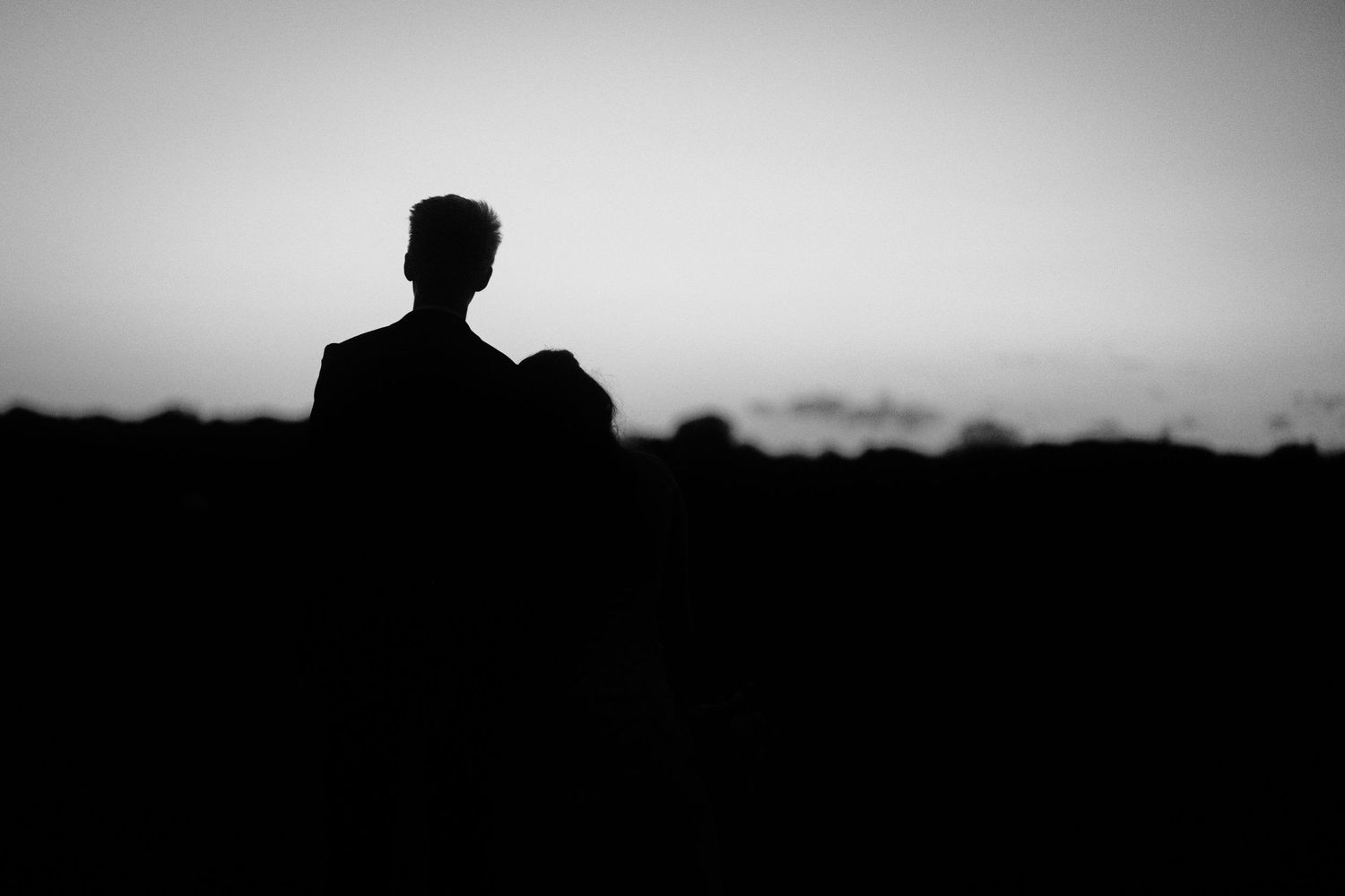 Silhouette of a man standing alone against a twilight sky in a dramatic black and white landscape photo.