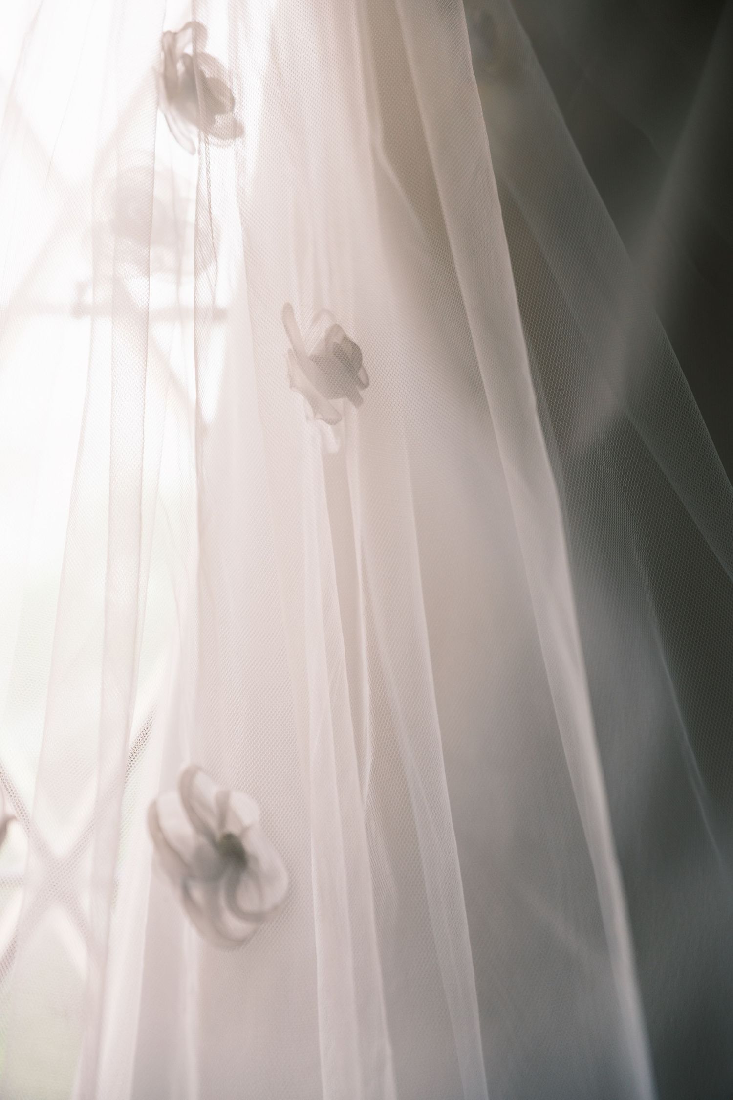 Delicate white bridal veil with floral appliques draped near a softly lit window.
