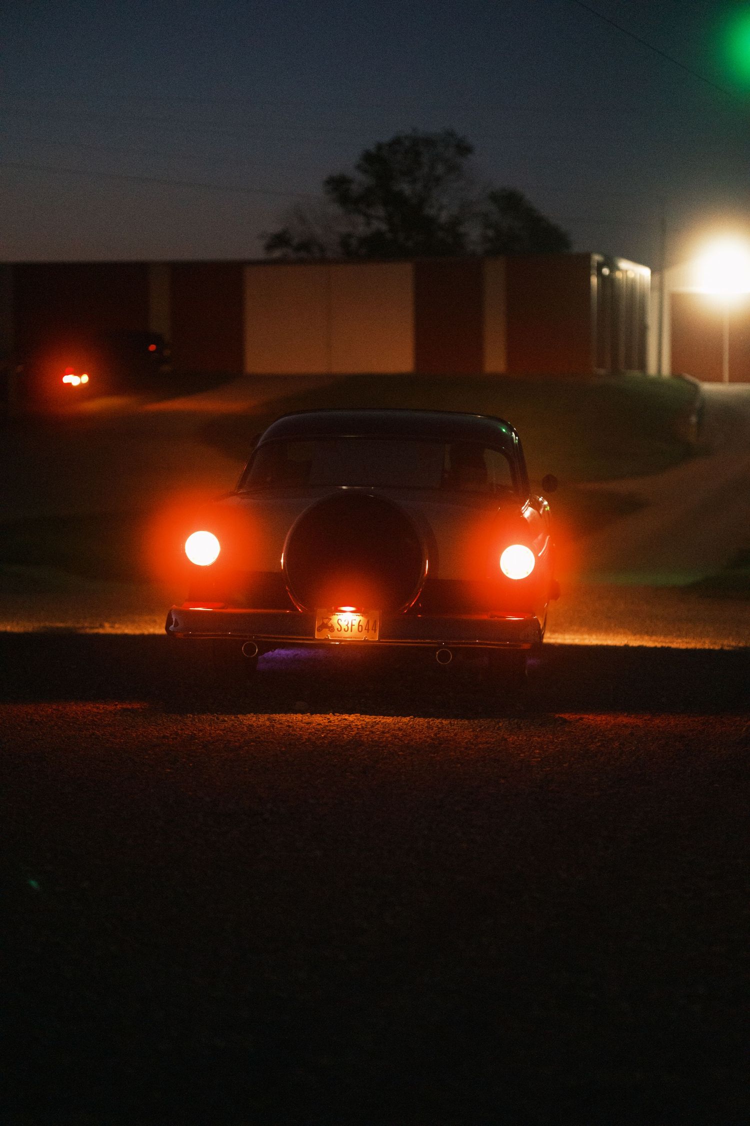 Vintage classic car with glowing red taillights parked on a dark road at night.