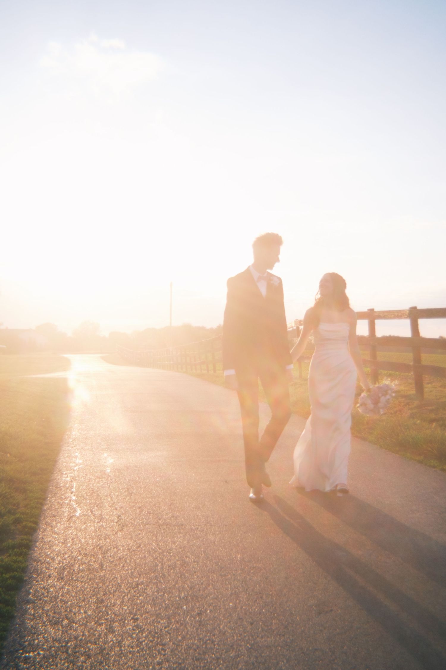 Bride and groom walking hand in hand down a sunlit path during golden hour at their outdoor wedding.