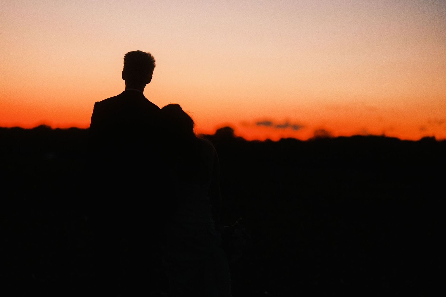 Silhouette of a couple embracing against a vibrant orange and red sunset sky outdoors.
