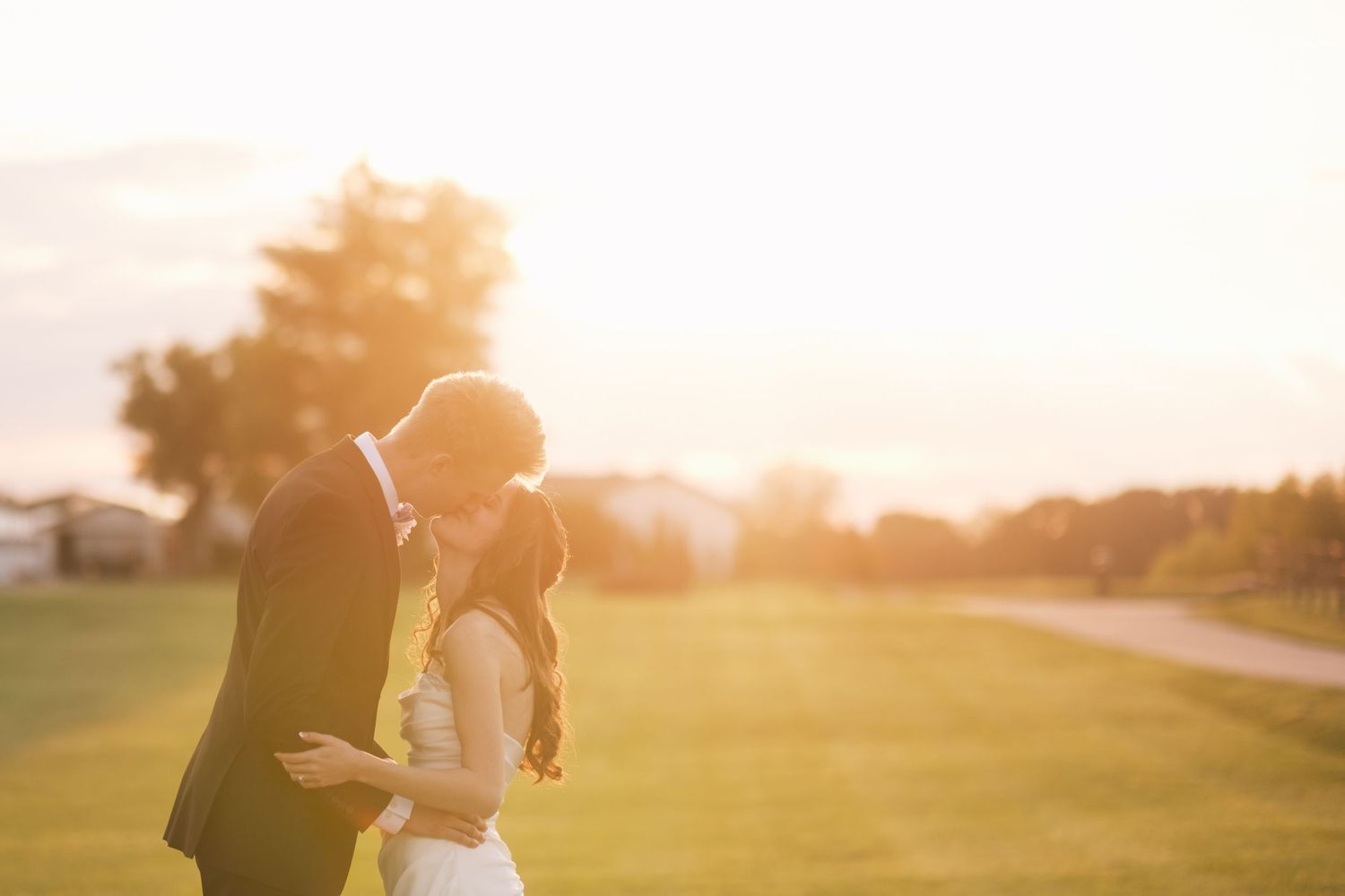 A bride and groom share a romantic sunset kiss on a lush green lawn during their outdoor wedding ceremony.