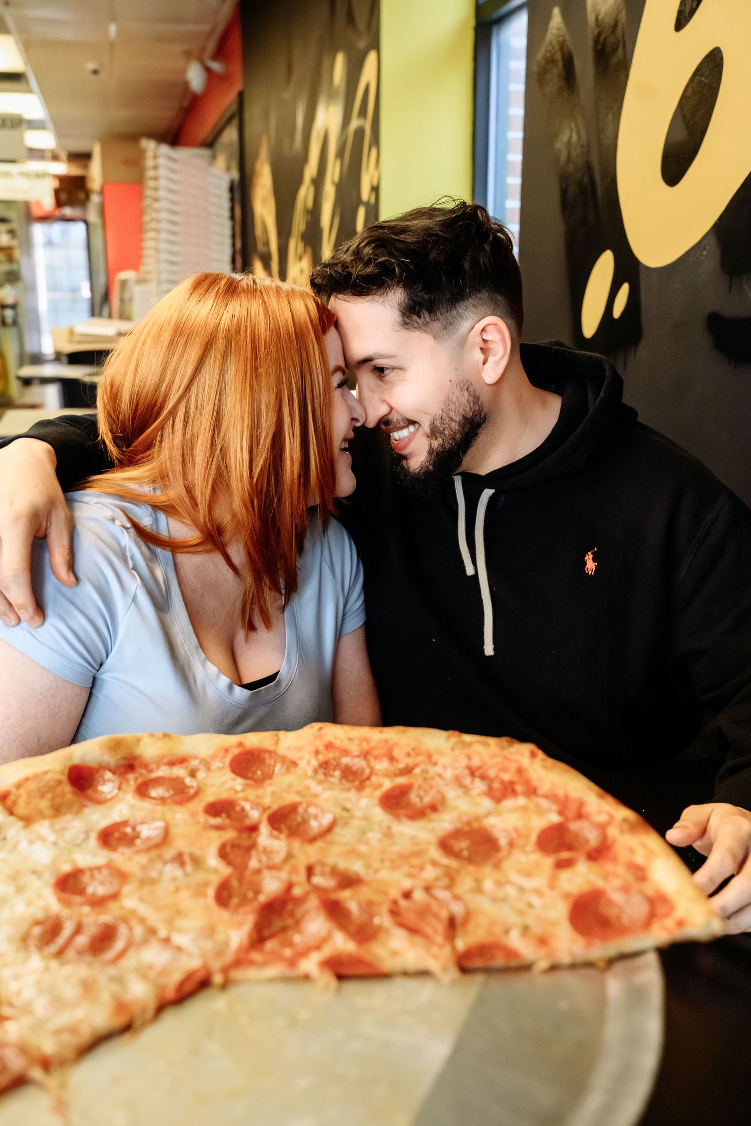 Happy couple snuggling close together at a restaurant table with a large pepperoni pizza in the foreground.