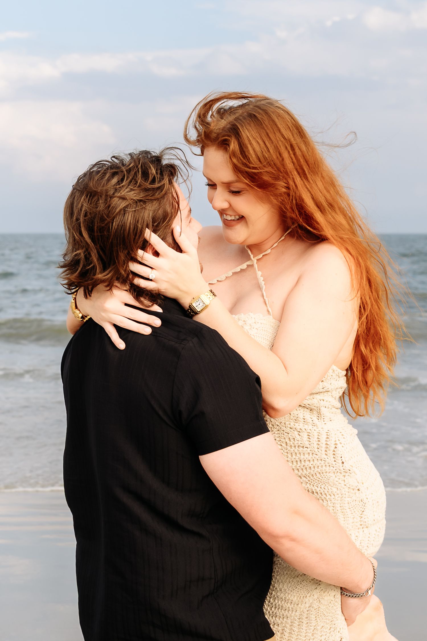 Couple embracing and smiling at each other on a beach, woman with long red hair.