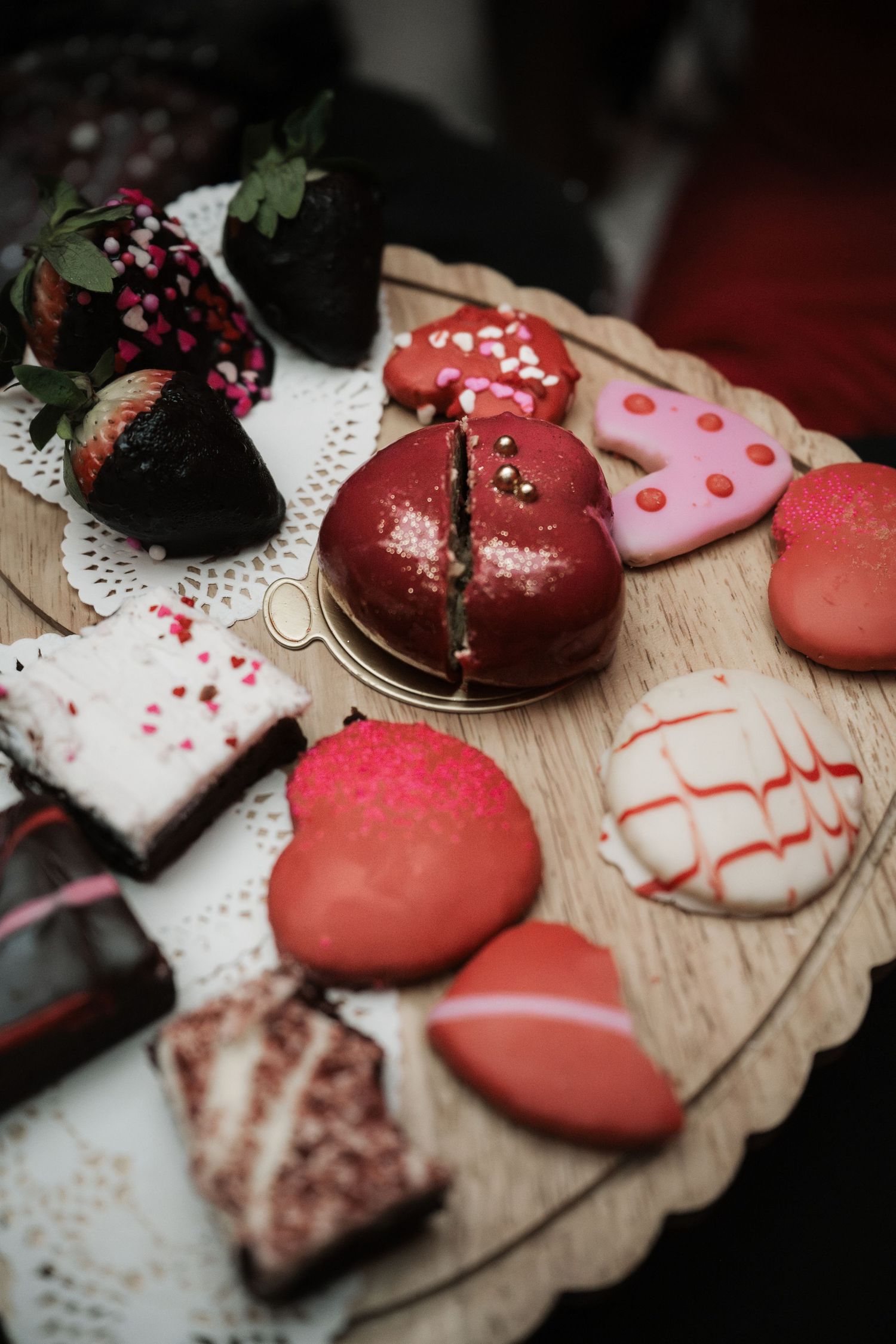 Valentine's Day dessert board with heart-shaped cookies, red velvet cake, macarons, brownies, and chocolate-covered strawberries.