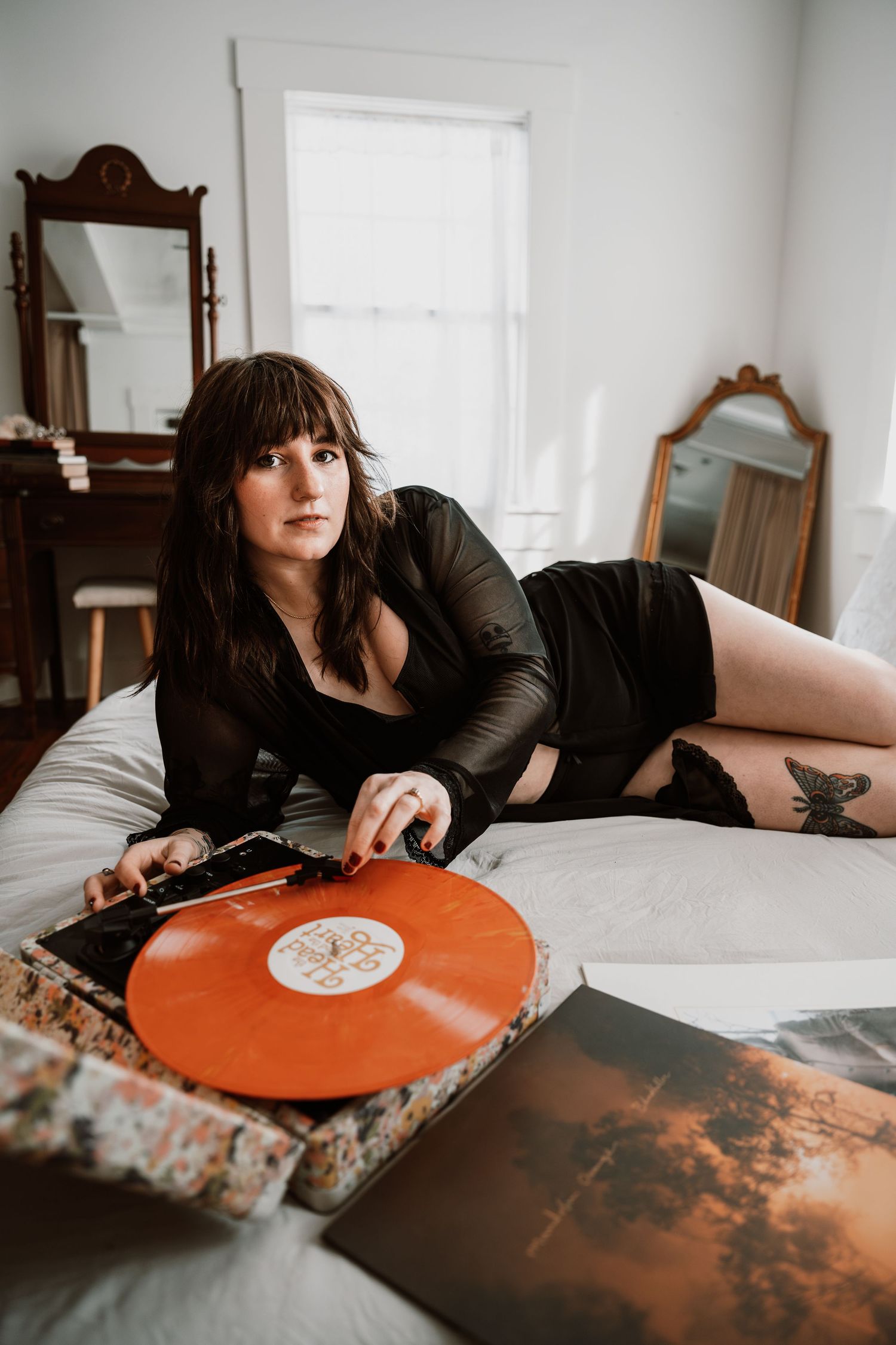 Woman in black lingerie poses on bed with orange vinyl record in vintage room.