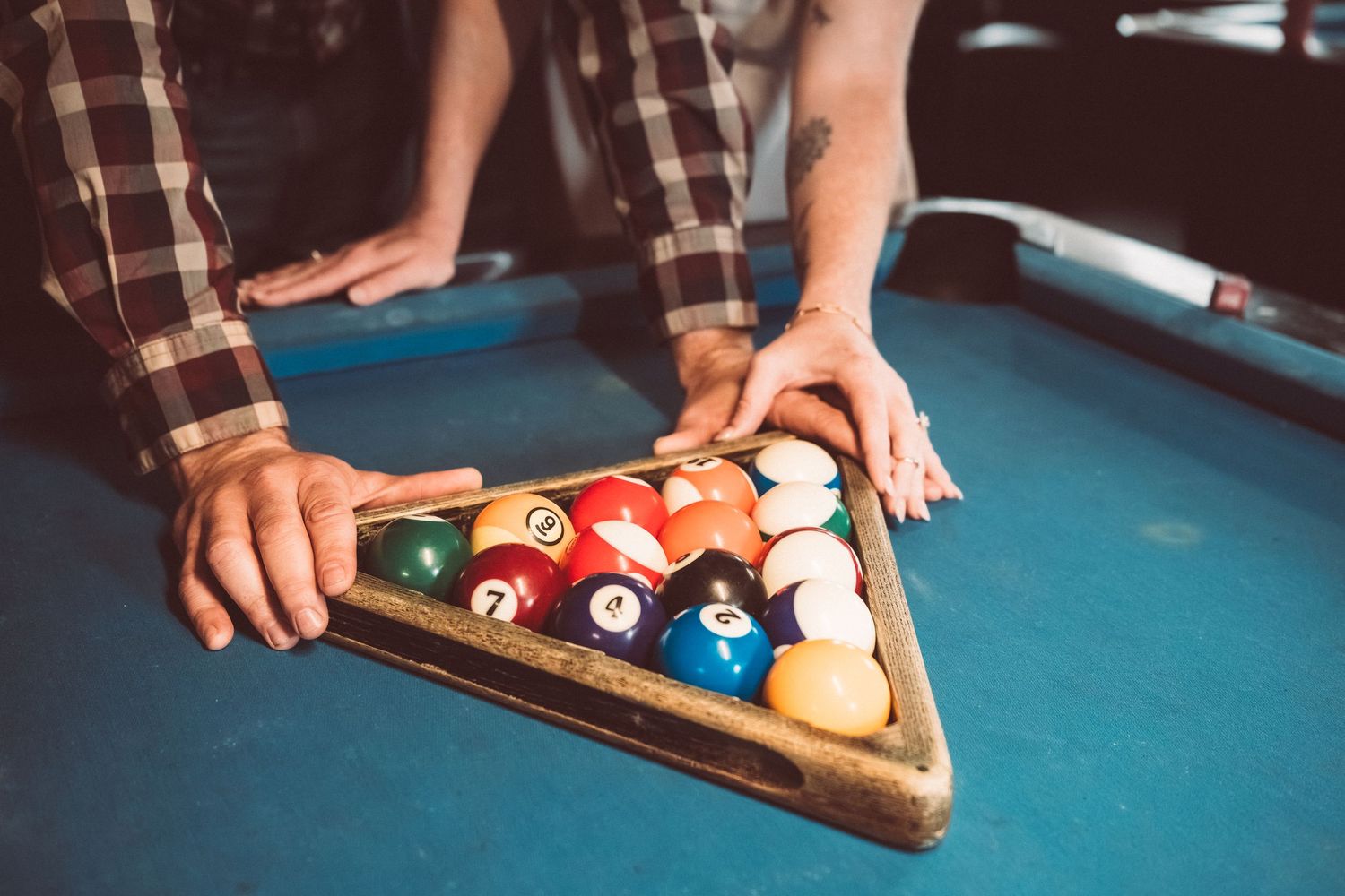 Hands setting up colorful billiard balls on a blue pool table for a game.