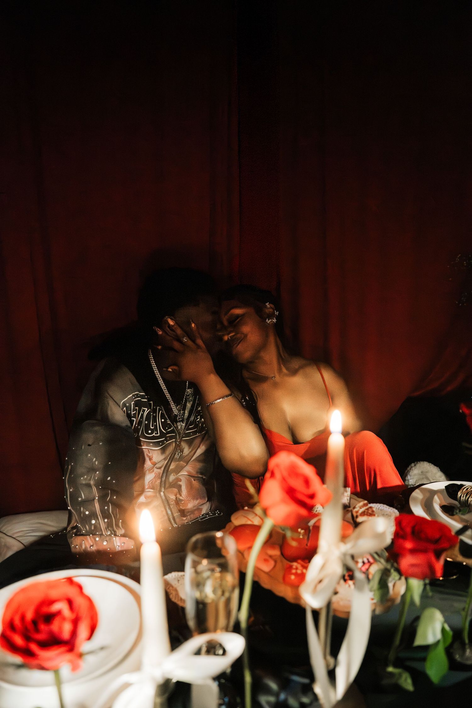 Couple shares intimate candlelit moment surrounded by red roses and champagne in romantic red tent.