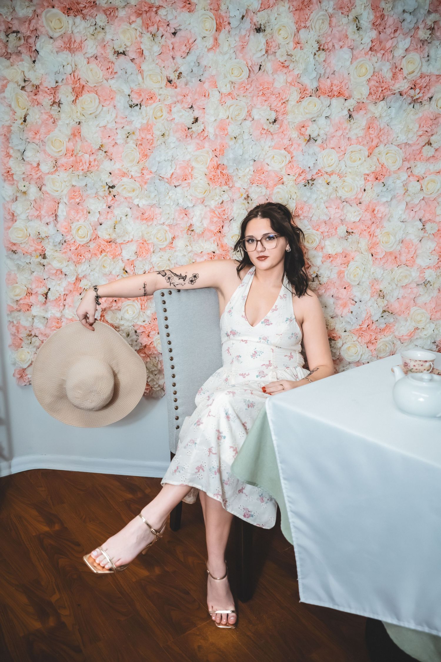 A figure in a white floral dress reclines on a couch against a pink floral backdrop in an elegant photo series.