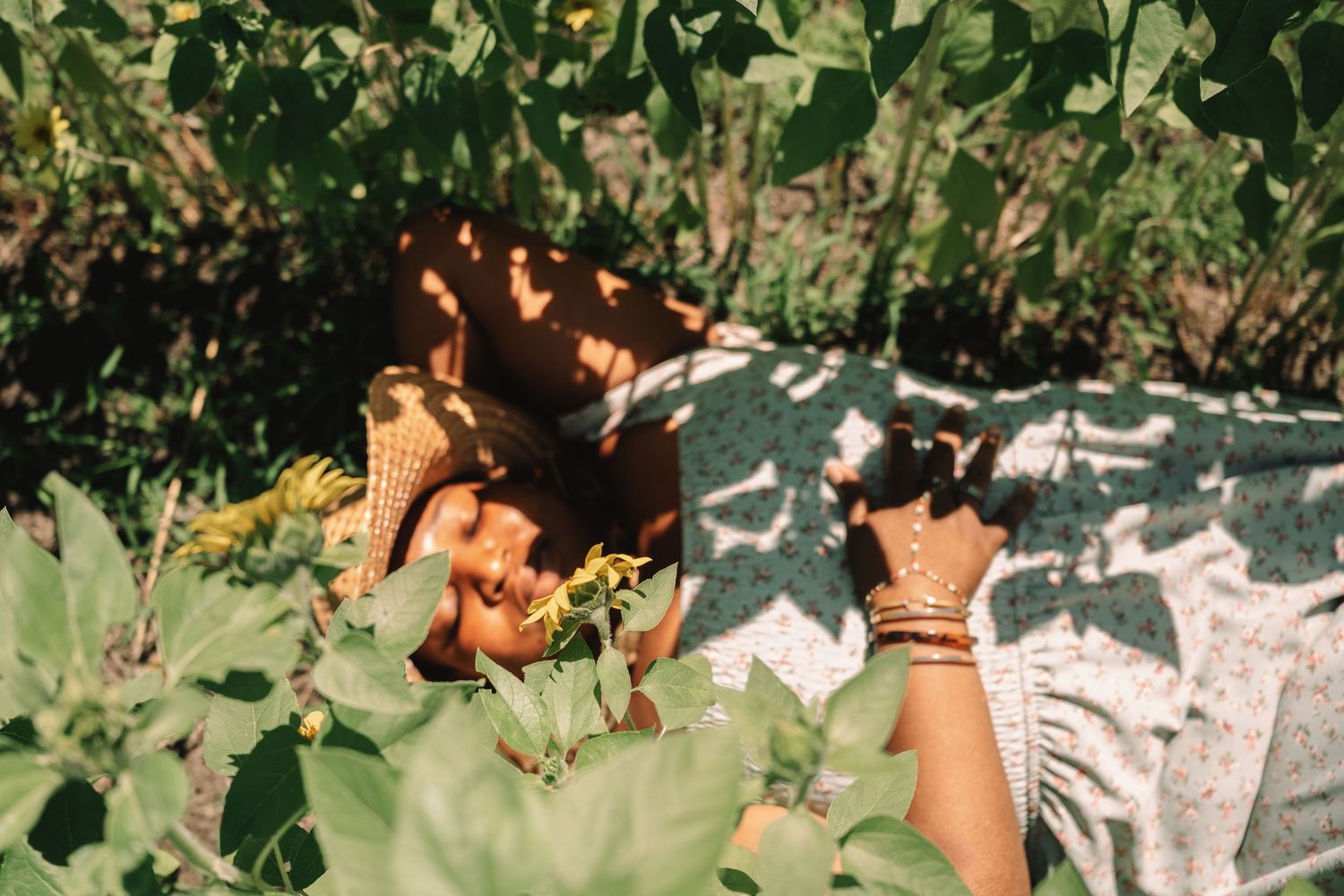 Woman lying on a blanket surrounded by lush green foliage, enjoying a peaceful sunny afternoon outdoors.