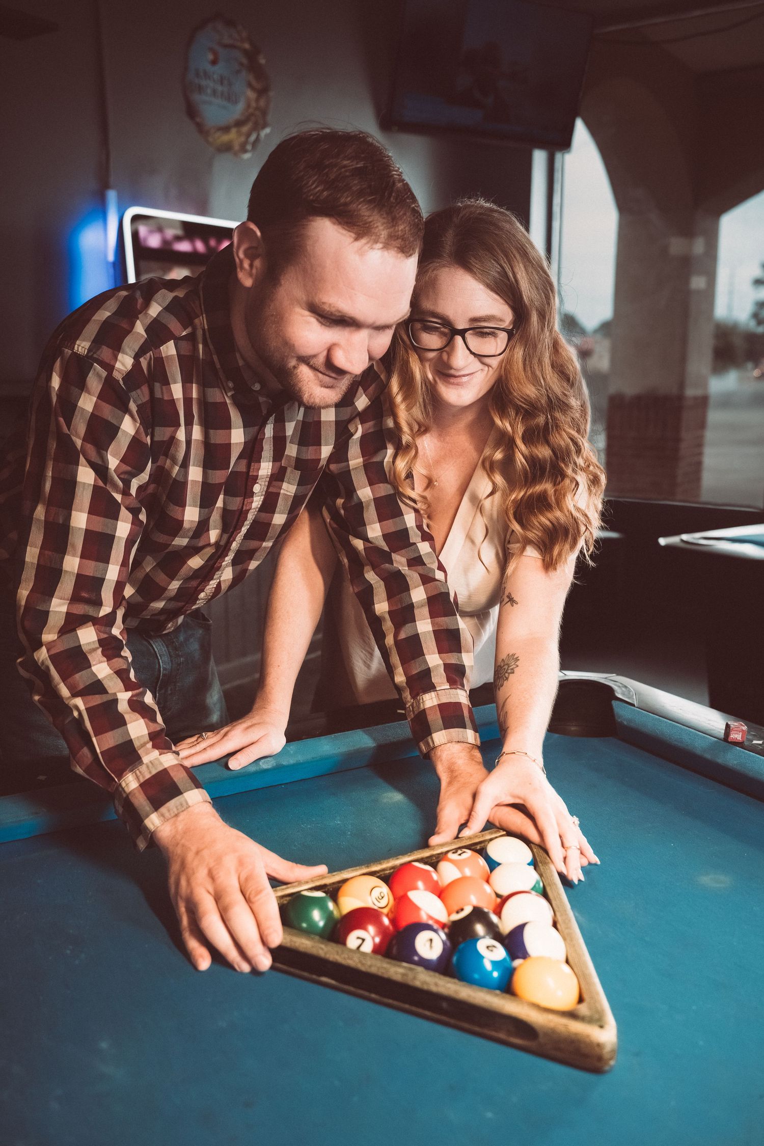 A couple enjoying a game of pool together as they rack up the billiard balls on a blue felt table.