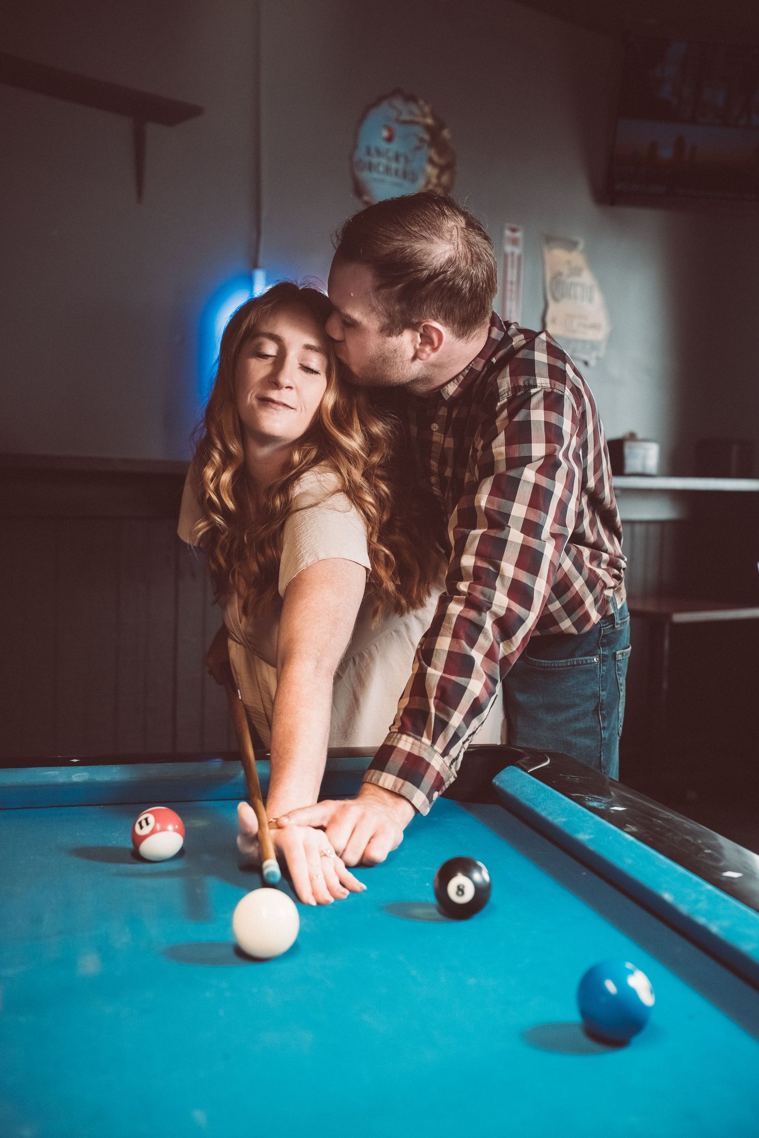 Couple sharing an intimate moment while playing pool at a dimly lit bar.