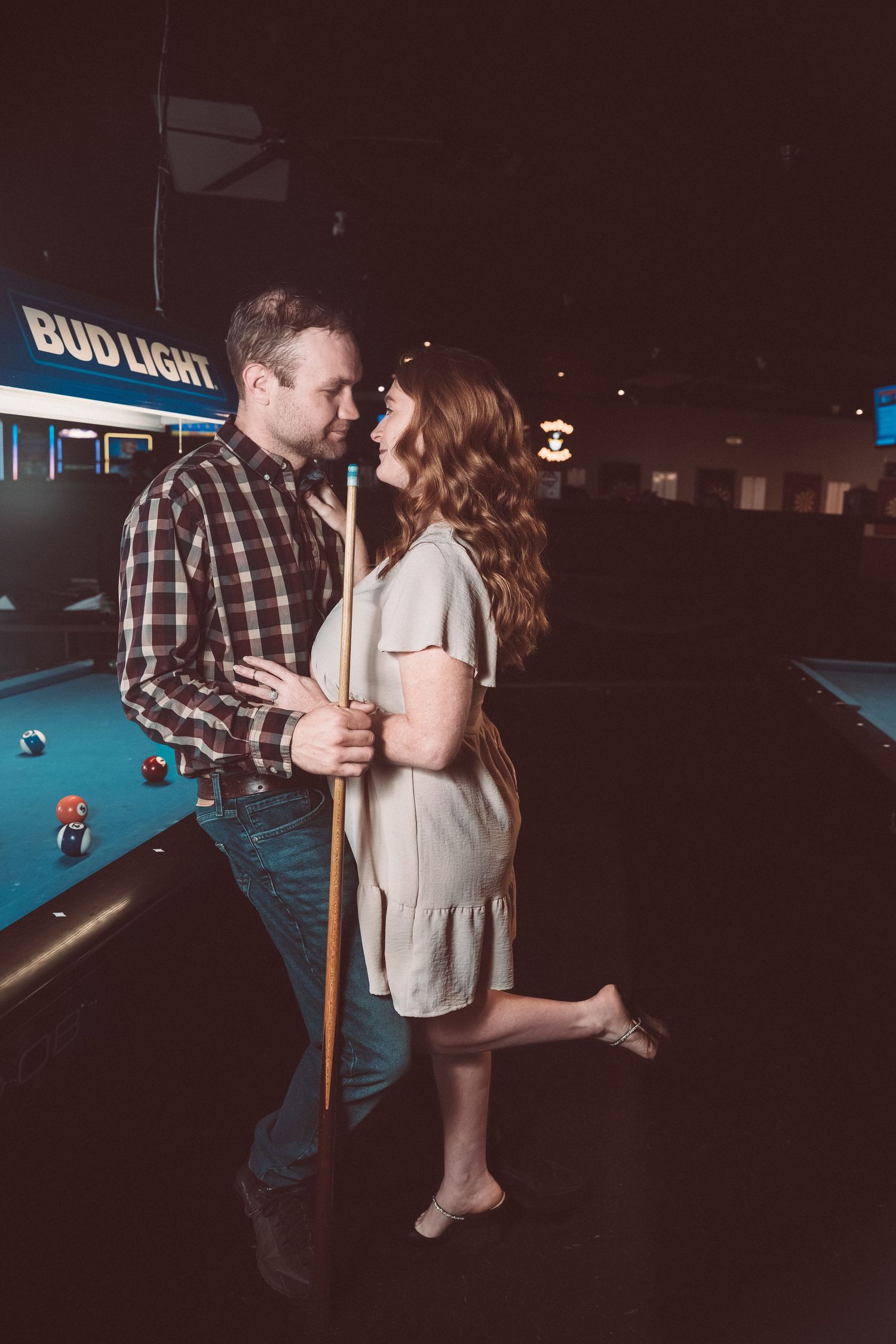 A romantic moment between a couple by a pool table in a dark bar setting.