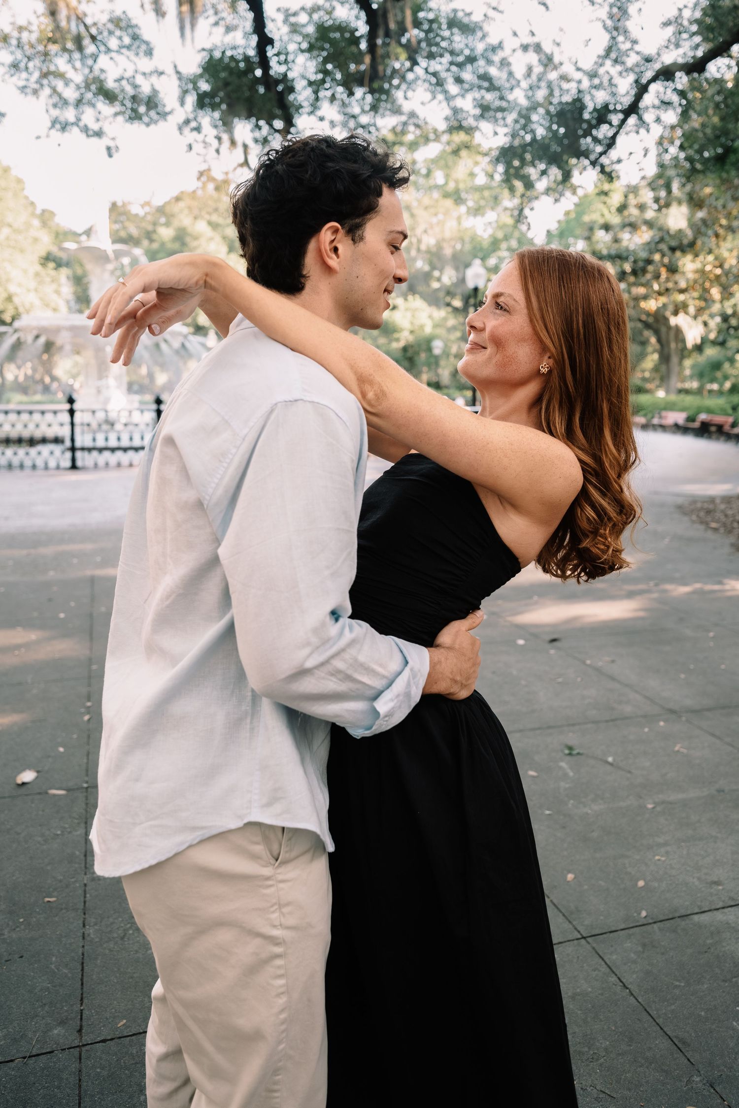 Happy engaged couple embracing and smiling at each other in a sunny outdoor park setting.